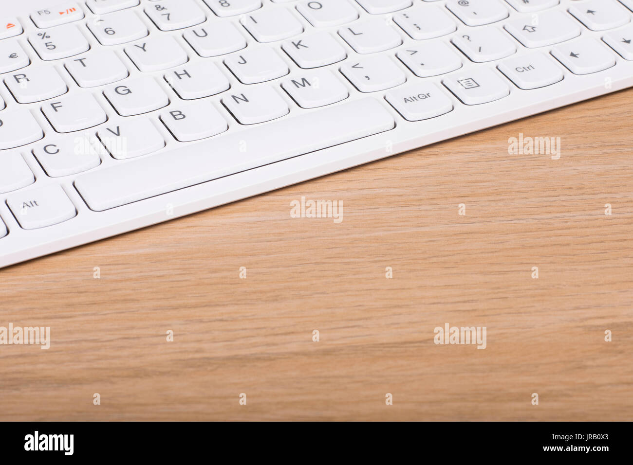 Calcolatore bianco tastiera su una scrivania di legno in una vista diagonale con copia spazio su woodgrain testurizzata Foto Stock