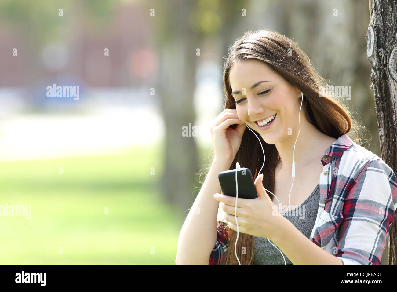 Happy girl ascolta on line di musica e la visione di contenuti multimediali in uno smart phone in un parco Foto Stock
