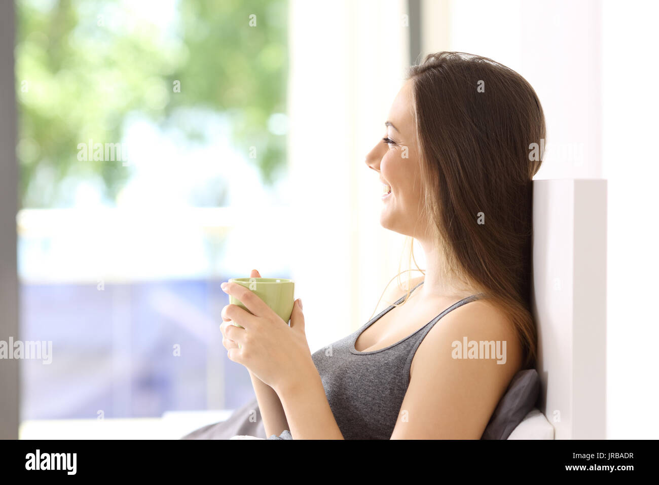 Vista laterale di un felice sola donna avente la colazione sul letto di una camera di hotel o appartamento Foto Stock