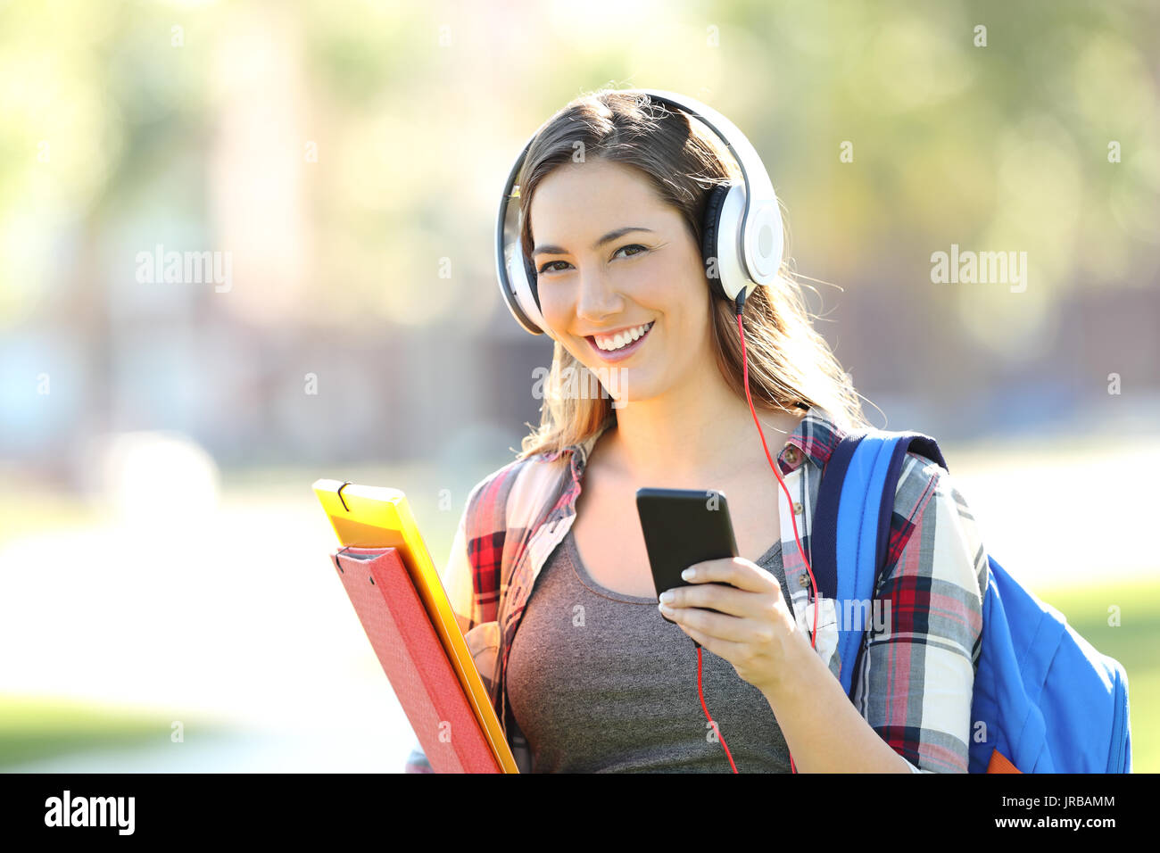 Bella studente che indossano le cuffie ascoltando musica e guardando a voi in strada Foto Stock