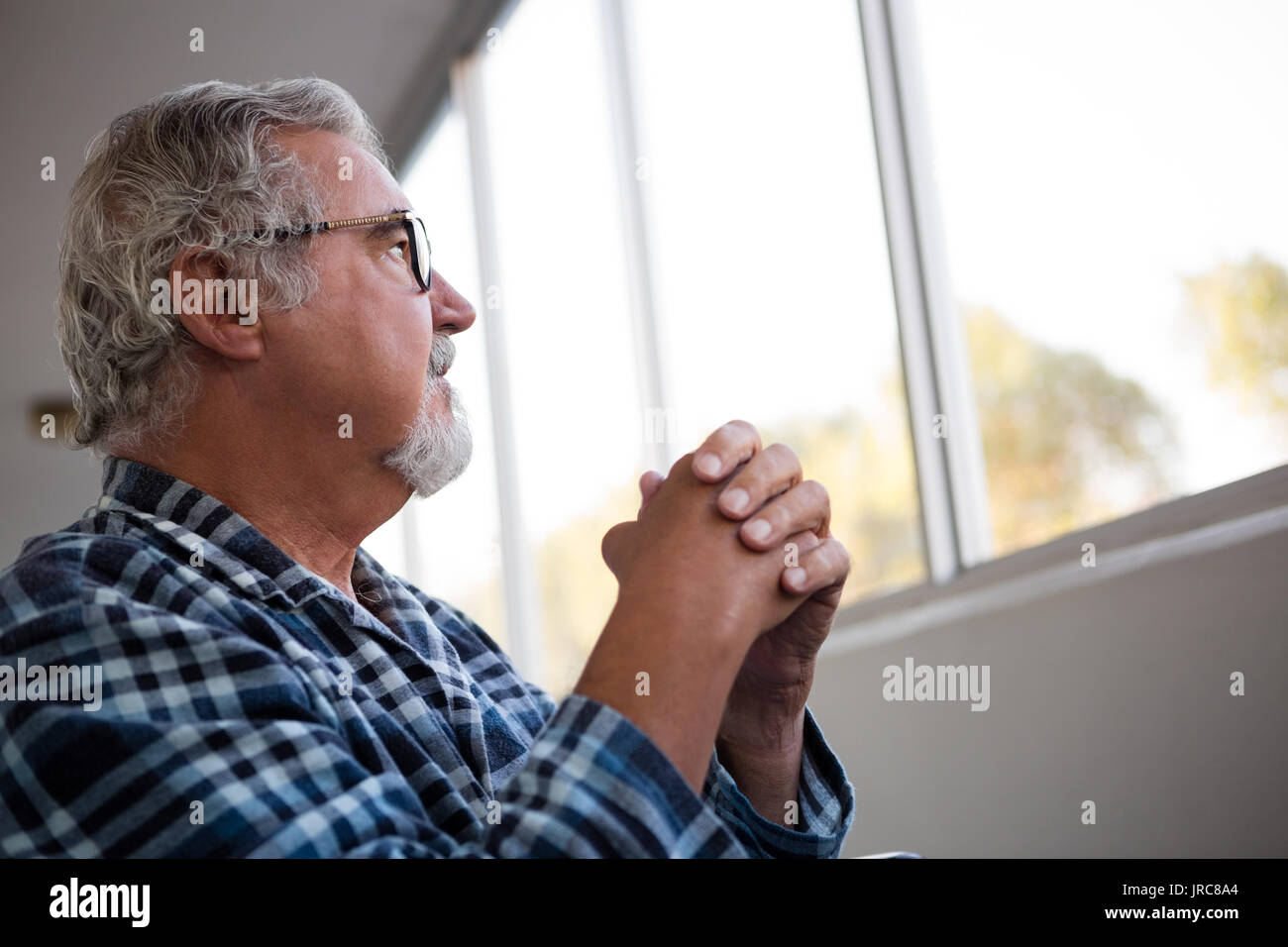 Riflessivo senior l uomo che guarda lontano mentre è seduto su una sedia a rotelle in casa di riposo Foto Stock