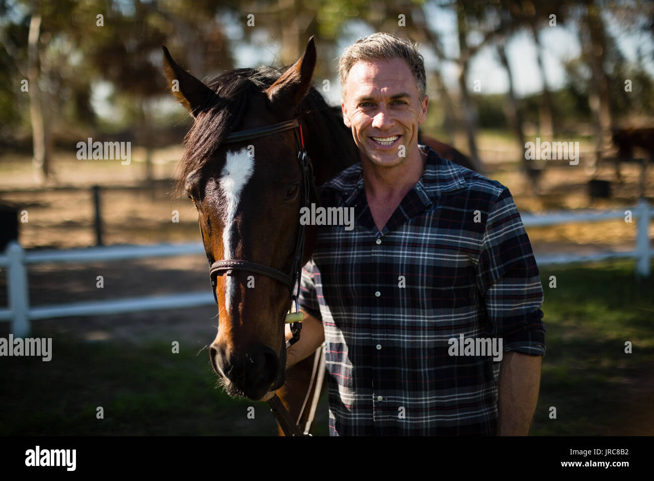 Uomo in piedi con cavallo al ranch in una giornata di sole Foto Stock