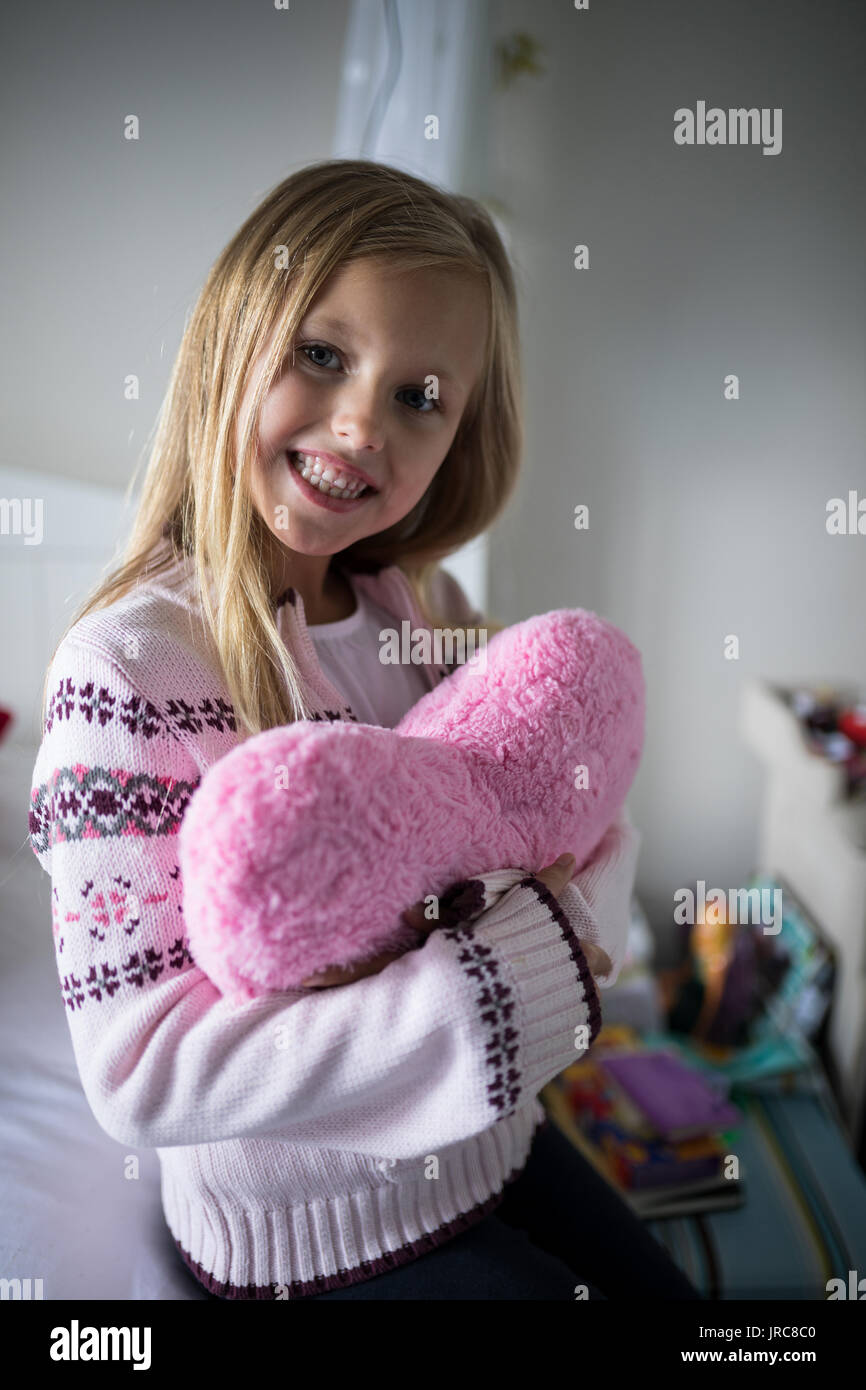 Ritratto di sorridente ragazza con forma di cuore cuscino sul letto in camera da letto Foto Stock