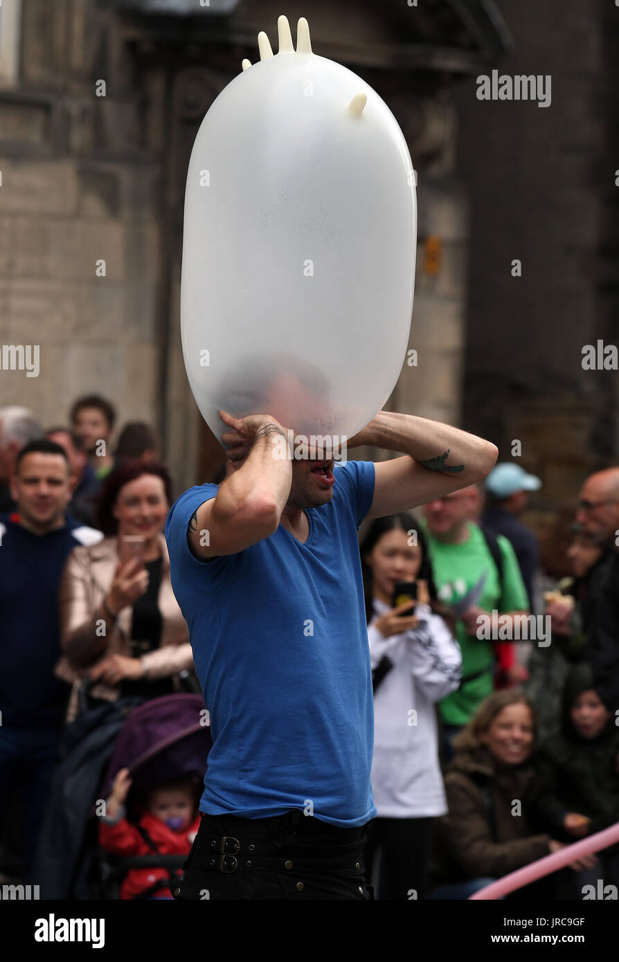 Street performer Figo indossa un guanto di gomma sulla sua testa durante il suo agire sul Royal Mile di Edimburgo, come la festa principale stagione ufficialmente si mette in modo in un anno fondamentale nella vita culturale della città. Foto Stock