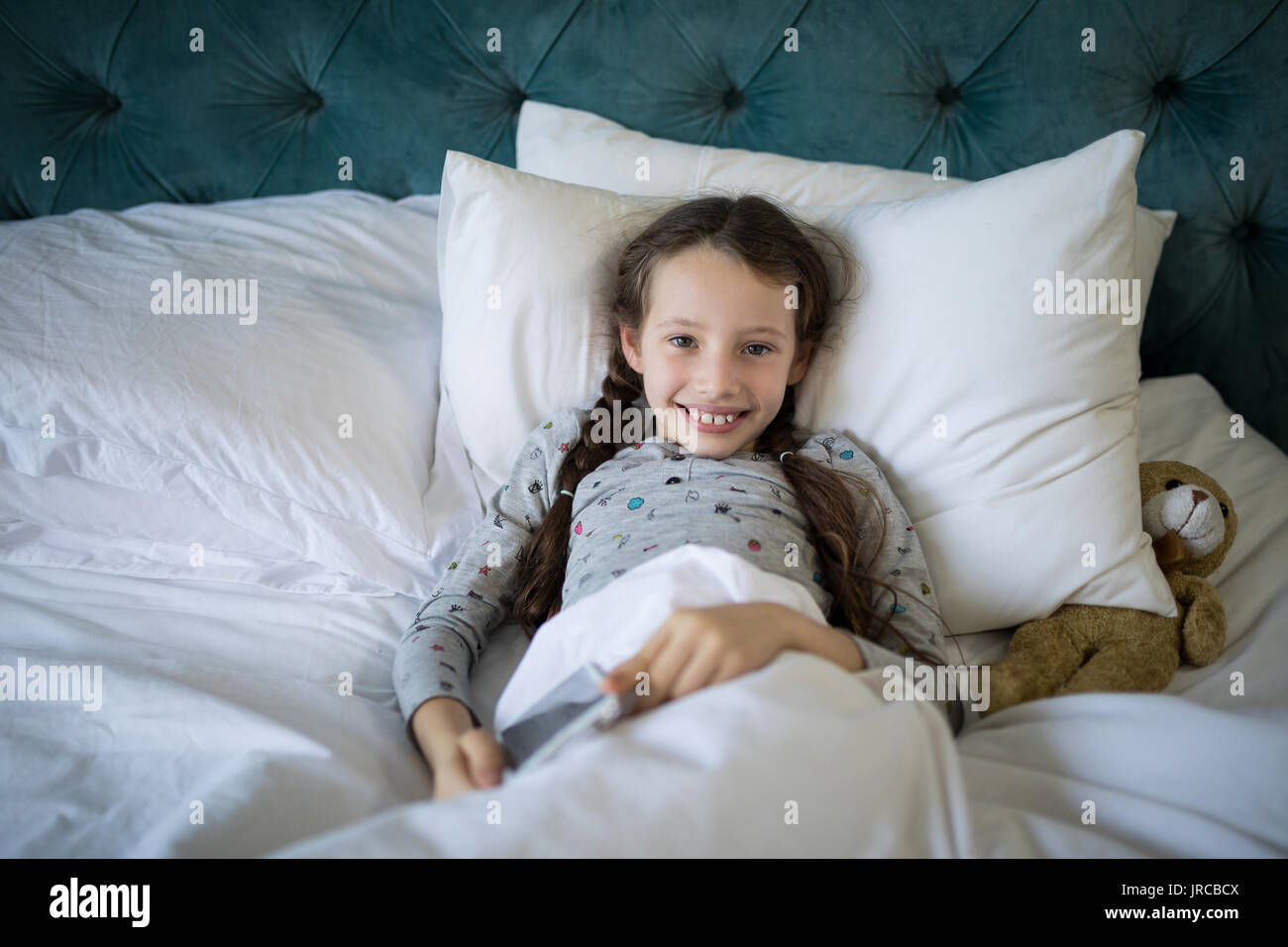 Ritratto di ragazza sorridente sdraiato sul letto con Teddy bear in camera da letto Foto Stock