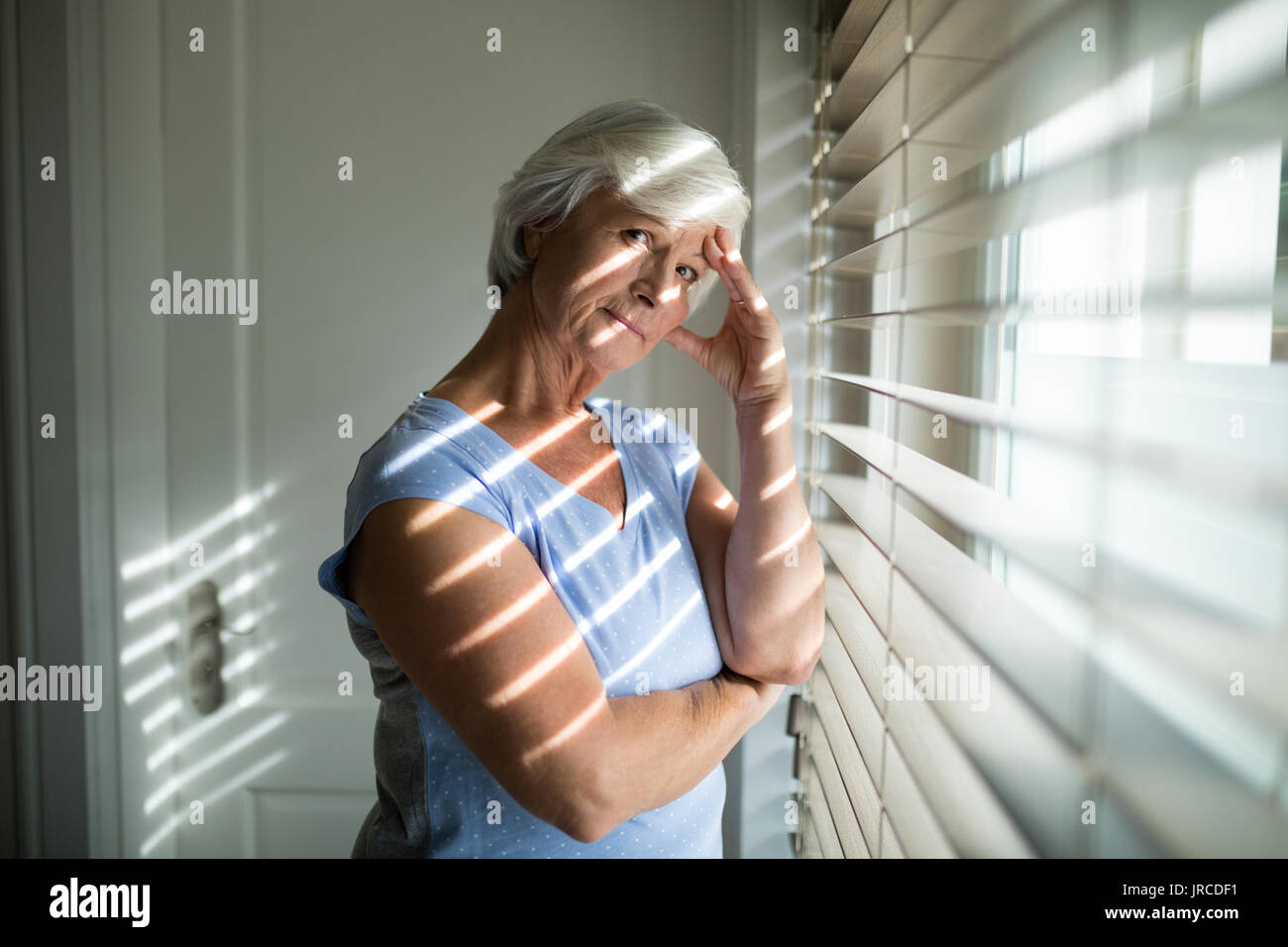 Ritratto di tesa senior donna in piedi vicino alla finestra in camera da letto a casa Foto Stock