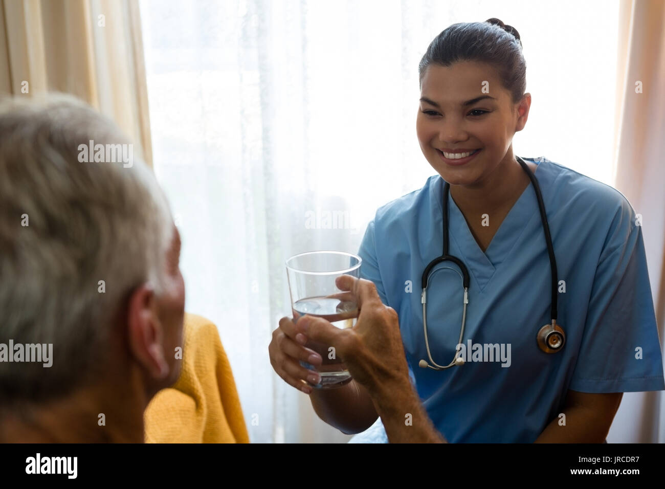 Medico donna dando acqua per uomo senior presso la casa di cura Foto Stock