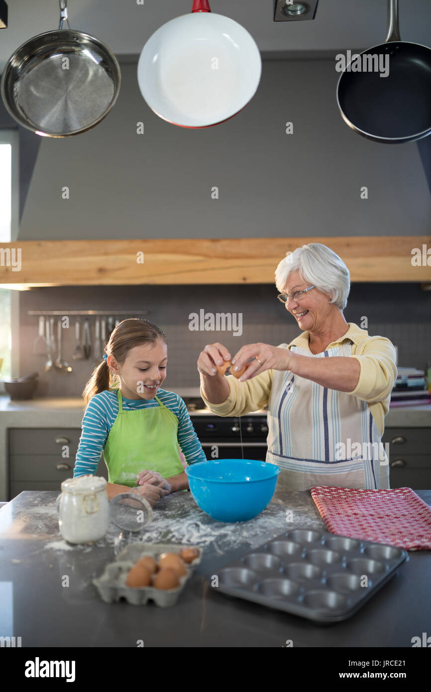 Nonna sorridente che mostra la nipote di rompere le uova in cucina Foto Stock