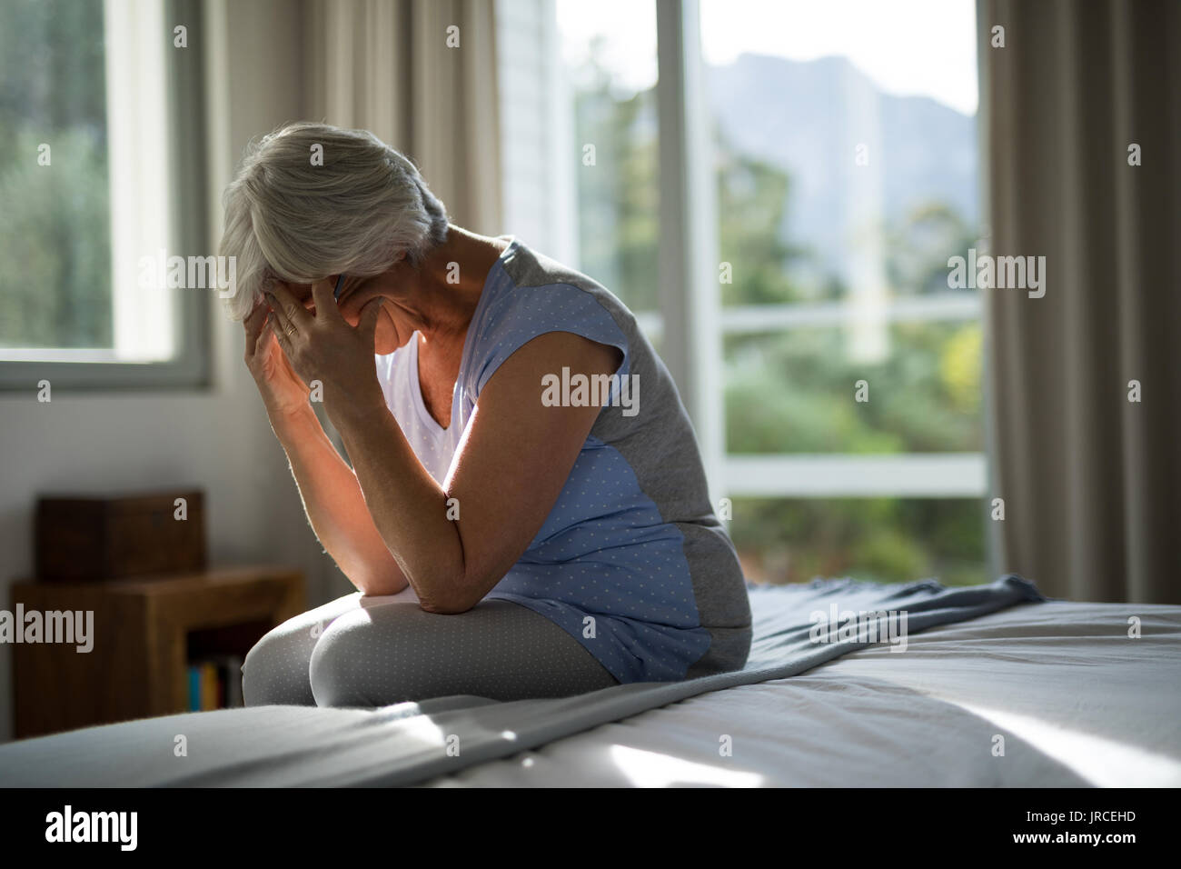 Tense senior donna seduta sul letto in camera da letto a casa Foto Stock