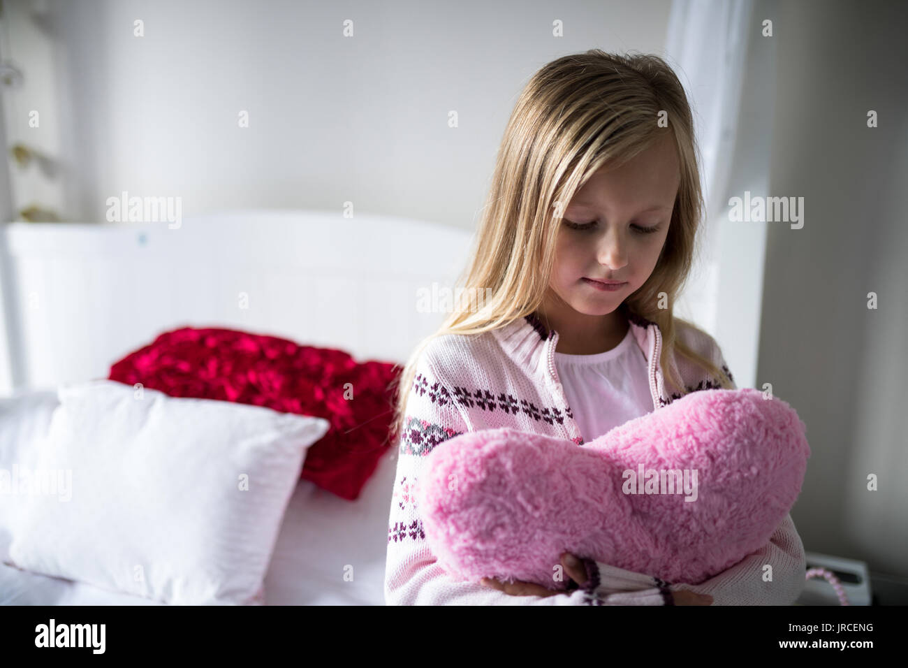 Ragazza con forma di cuore cuscino sul letto in camera da letto Foto Stock