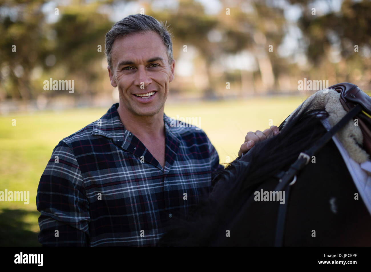Uomo in piedi con cavallo al ranch in una giornata di sole Foto Stock