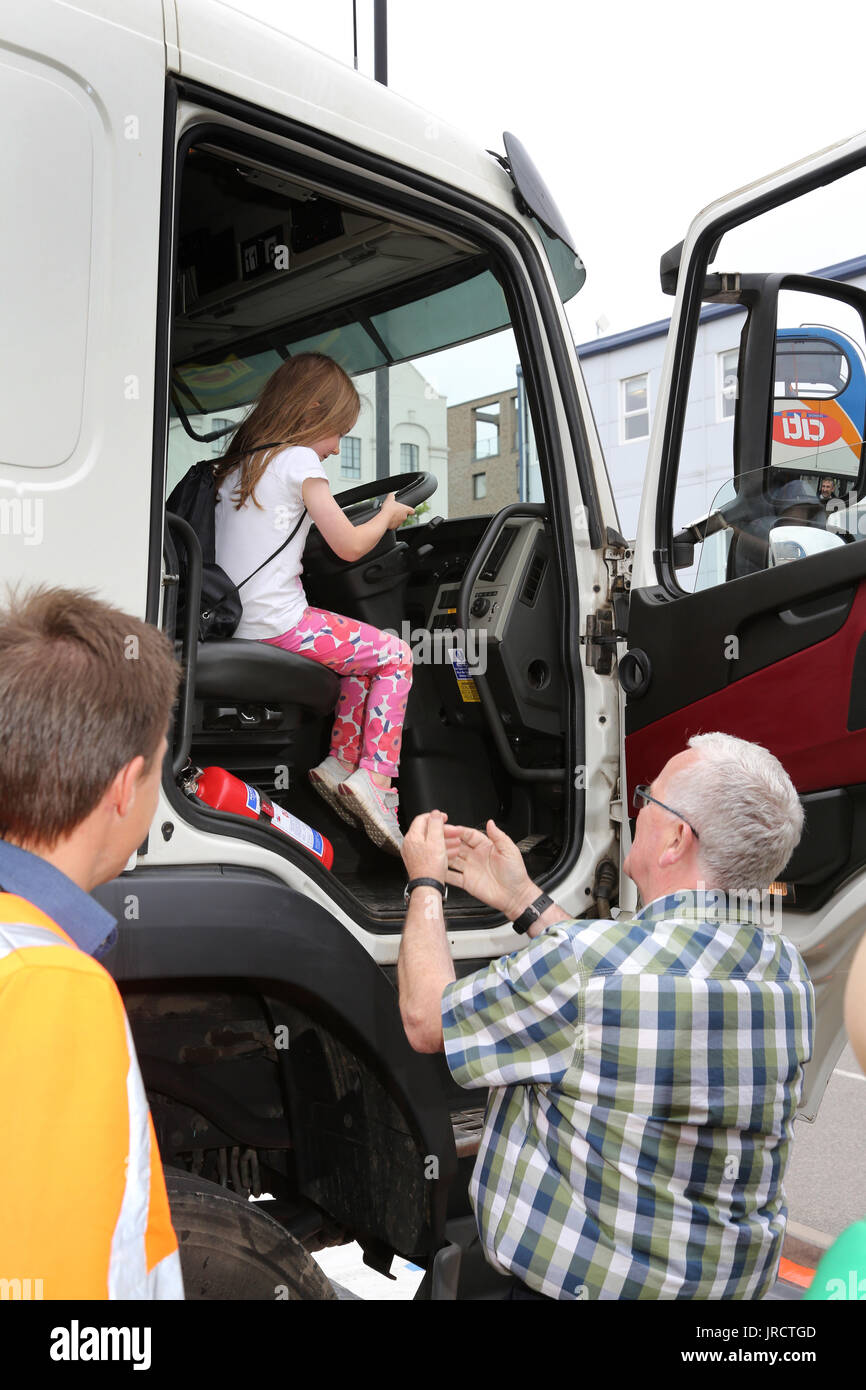 Una giovane ragazza si siede nel sedile di guida di una grande cabina del camion ad una strada di dimostrazione di sicurezza mentre il suo nonno e il camionista a guardare. Foto Stock