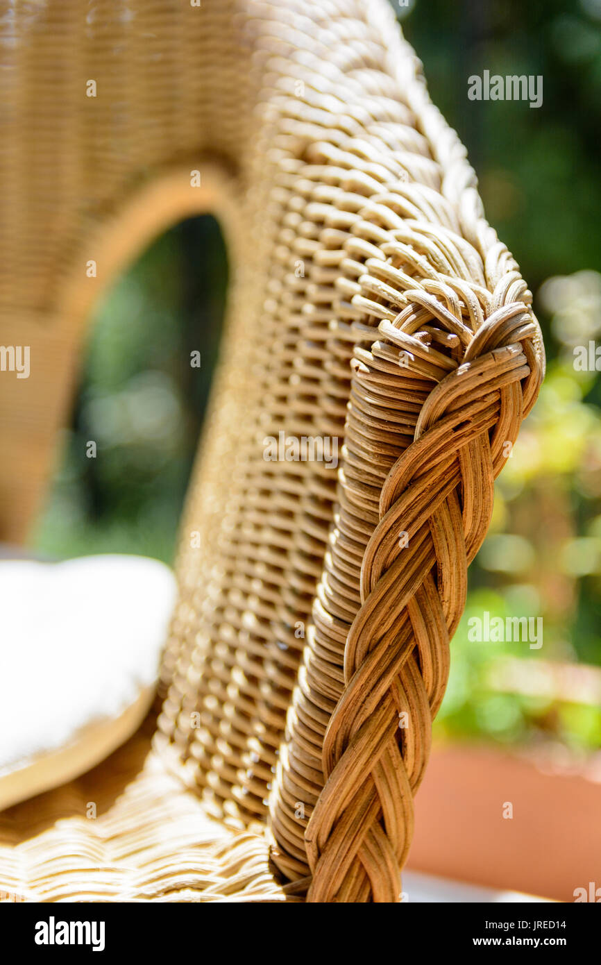 Vista ravvicinata sul bracciolo di una poltrona in rattan con cuscino bianco alla luce del sole su un balcone con piantatrice. Foto Stock