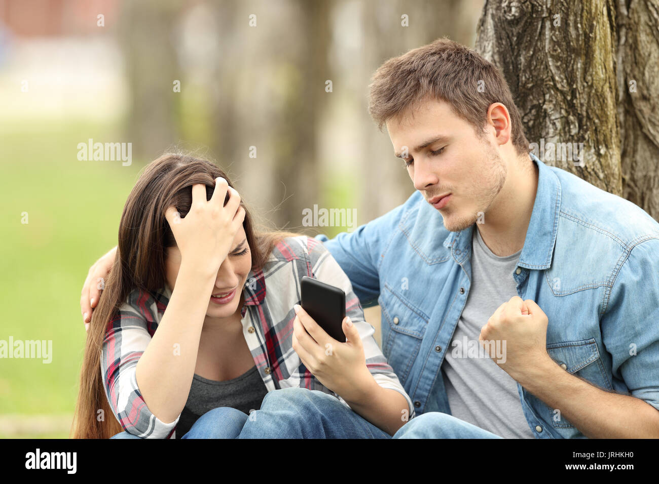 Felice ragazzo che celebra il suo triste amico è rompendo da chat seduta sul prato di un parco Foto Stock