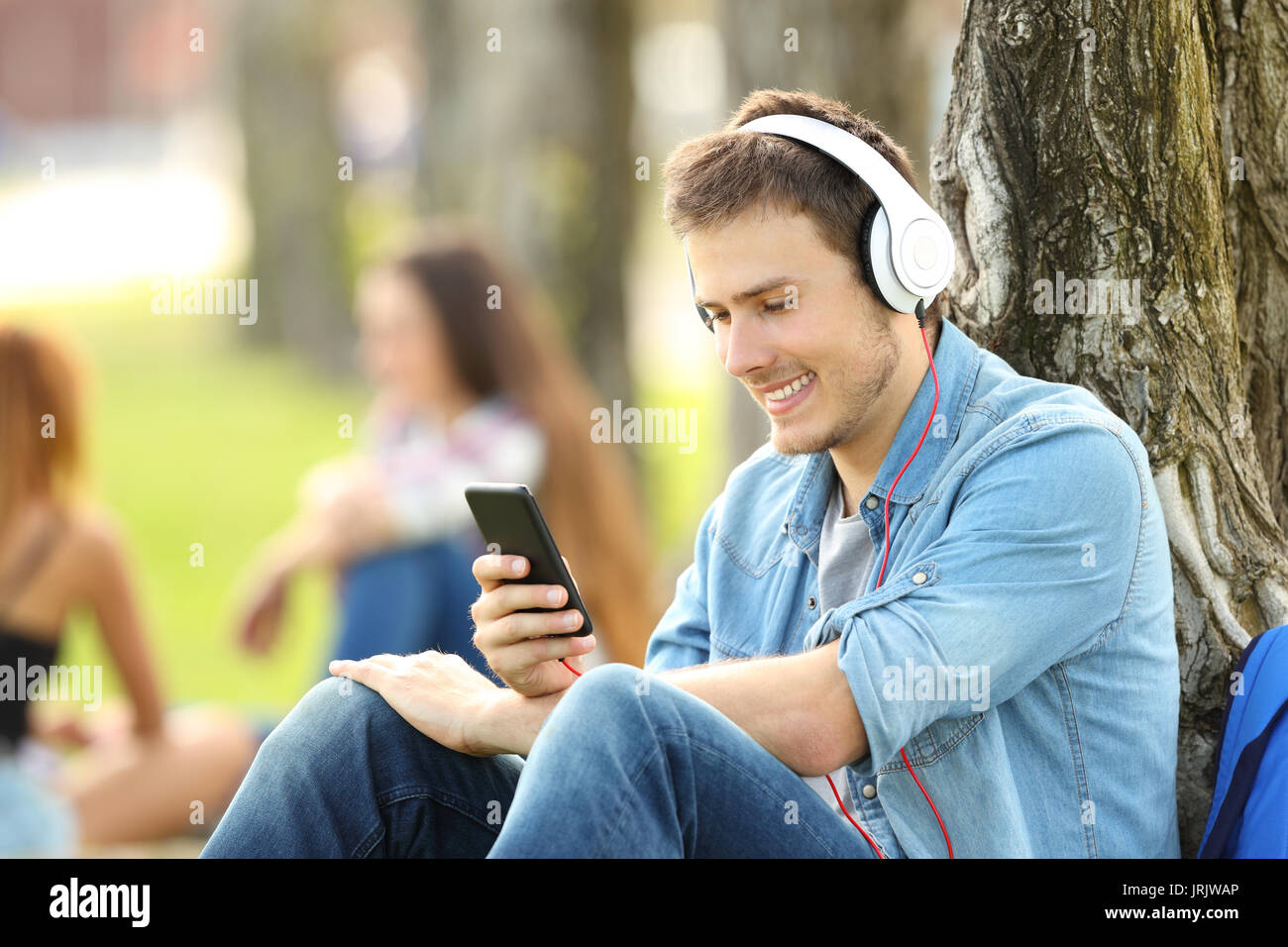 Lo studente ascolta la musica con le cuffie in un parco seduta sul prato di un parco Foto Stock