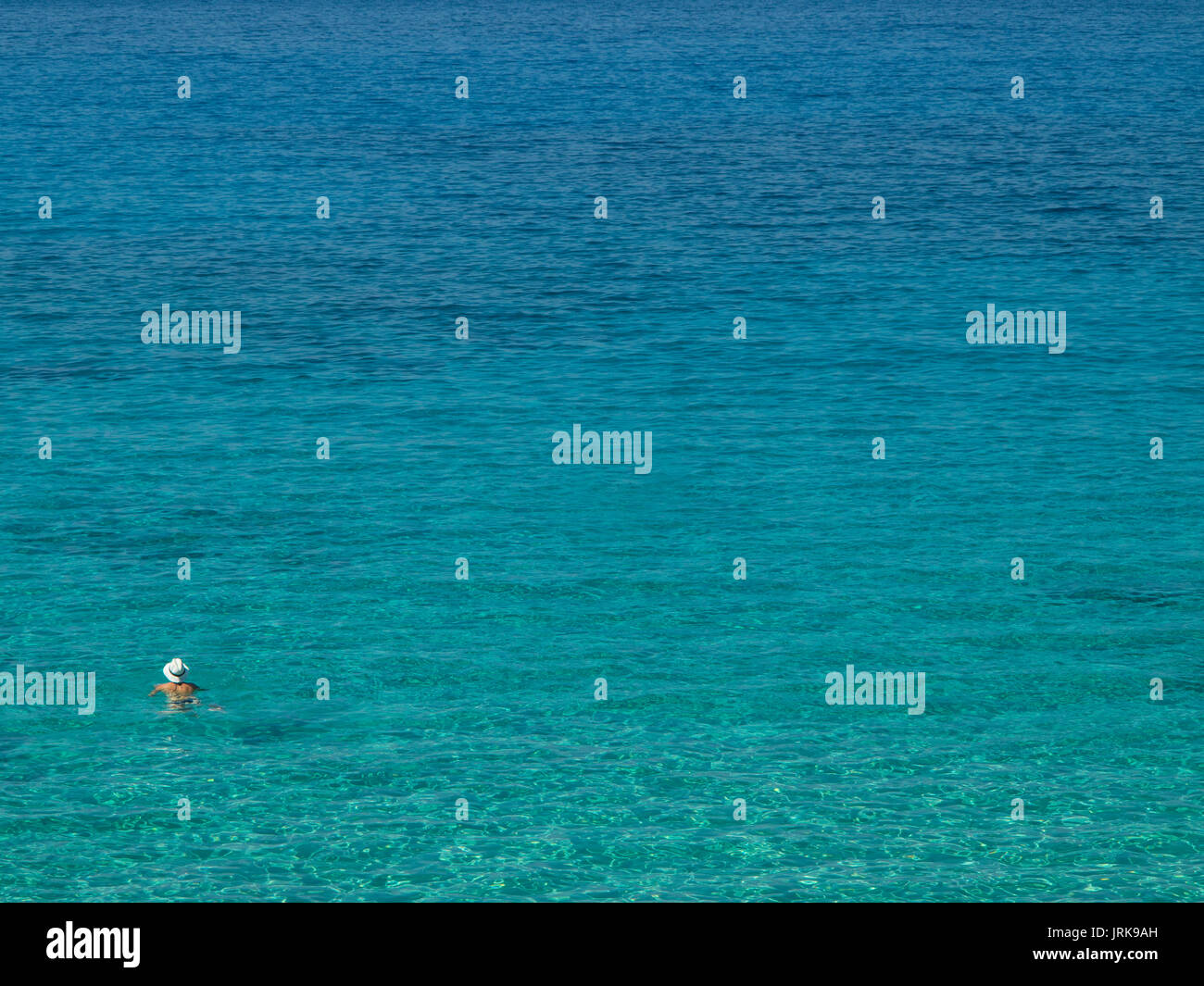 Una persona solitaria nuota in un mare azzurro con un cappello di paglia sul Foto Stock