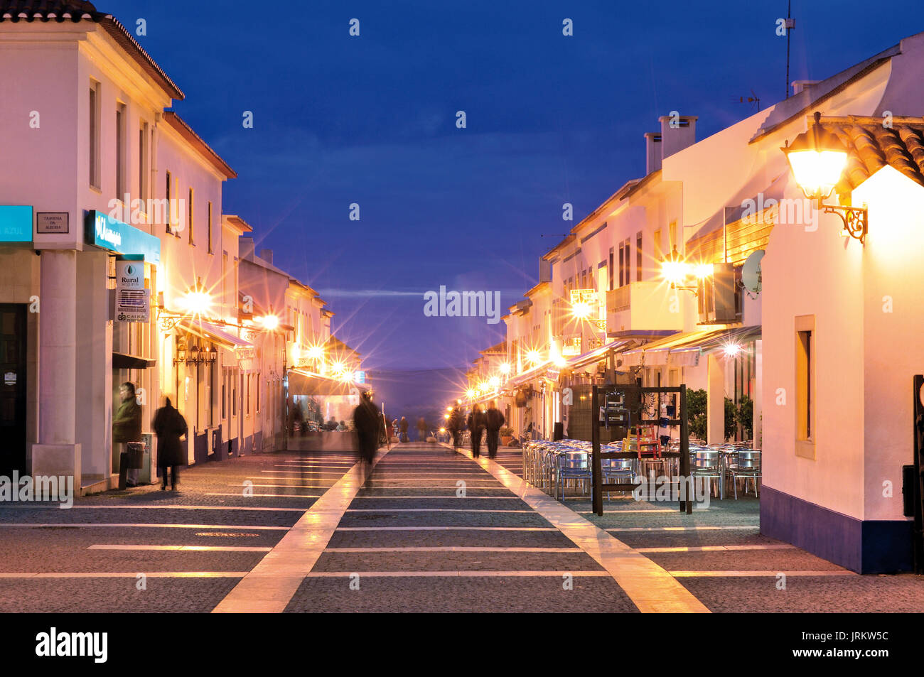 La gente camminare lungo noctural illuminato la strada principale in un affascinante villaggio costiero Porto Covo Foto Stock