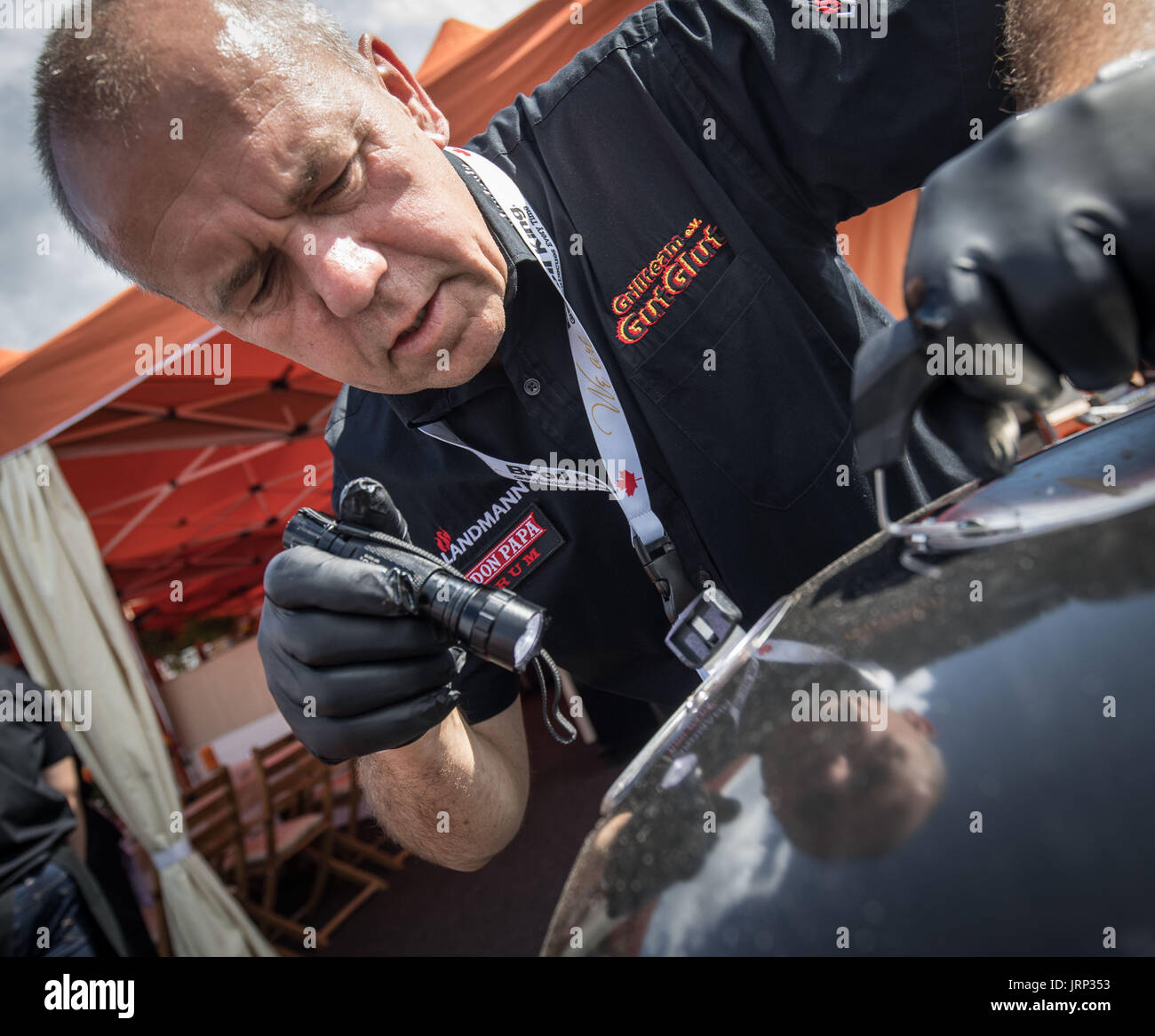 Thomas Pretsch, dal team di Michael Hoffmann da Rosrath, il campione in carica, guarda con una lampada tascabile attraverso una apertura nella griglia di copertura per verificare se le patate per un piatto di lato sono pronti durante il tedesco campionato Grill a Fulda, Germania, 06 agosto 2017. Circa 40 squadre sono in lizza per la corona grill a Fulda il Fair Grounds. Una giuria di circa 130 membri giudicare le diverse voci. L'evento organizzatore, il tedesco Barbecue Association, è di attribuire un prezzo di 11,300 euro al vincitore. Foto: Frank Rumpenhorst/dpa Foto Stock