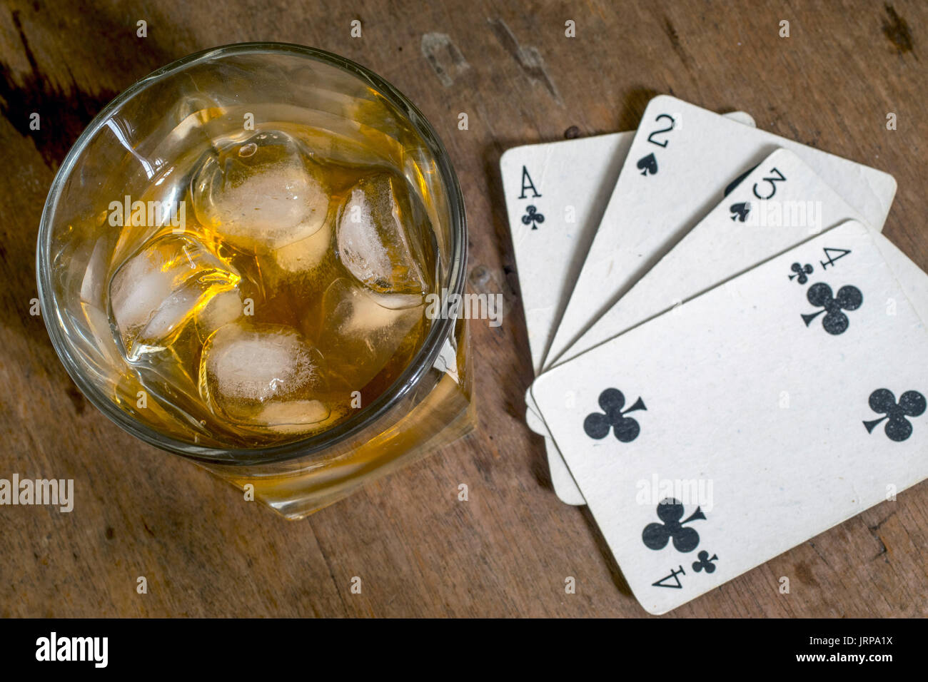 White carte da gioco, un bicchiere di whiskey con ghiaccio, sulla parte superiore di una tavola di legno Foto Stock