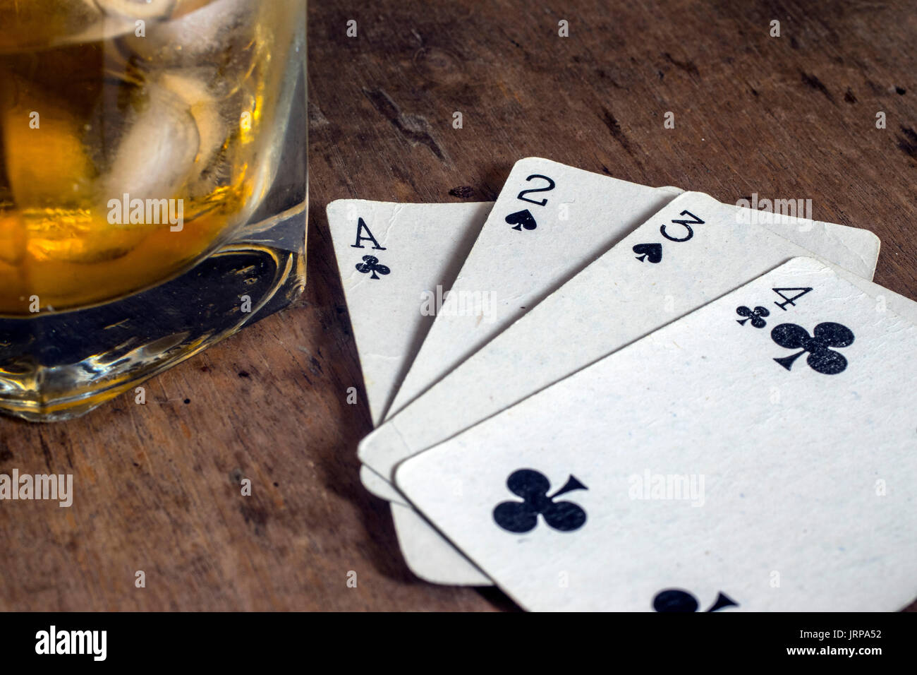 White carte da gioco, un bicchiere di whiskey con ghiaccio, sulla parte superiore di una tavola di legno Foto Stock