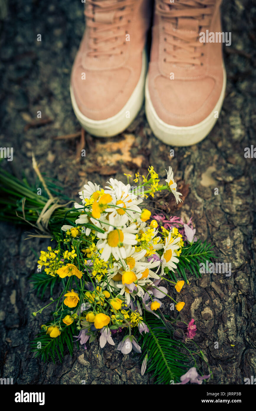 Bouquet di fiori selvatici fiori di primavera che giace vicino a piedi femminili. Bouquet di fiori di campo sulla corteccia di albero, in corrispondenza di una ragazza piedi - vista rustico Foto Stock