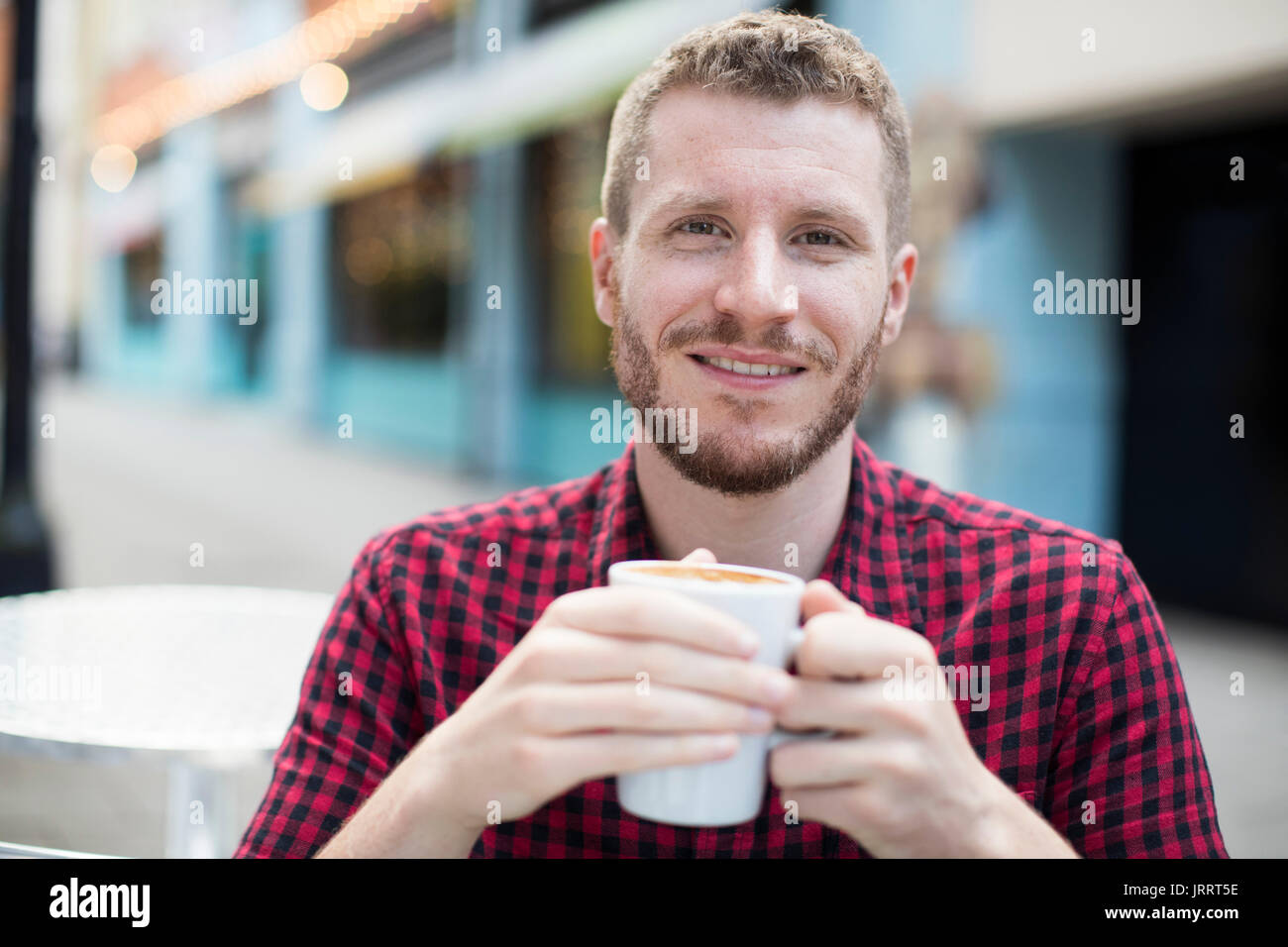 Ritratto di giovane uomo bere il caffè in Outdoor Cafe tabella Foto Stock