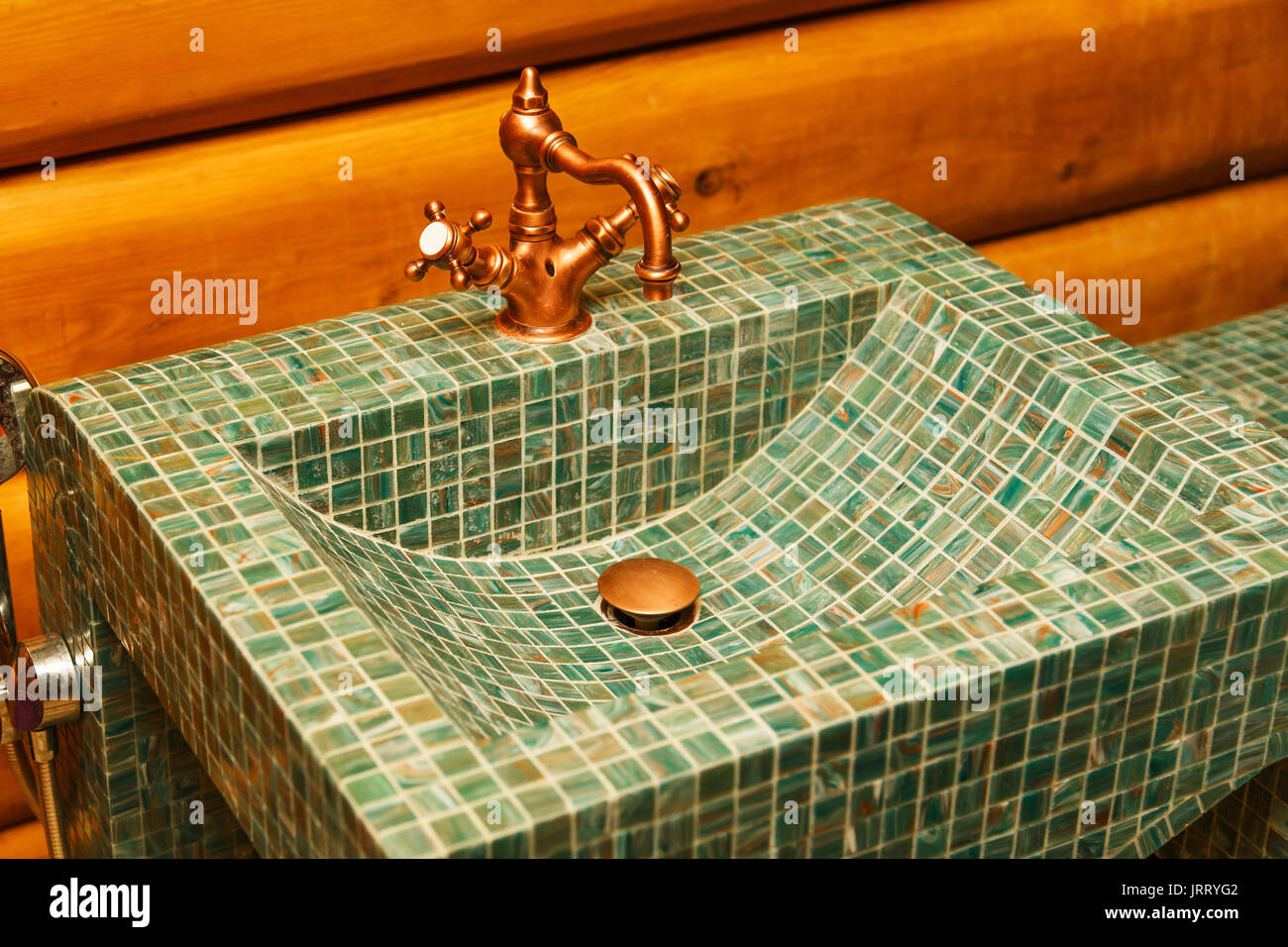 Il rubinetto di rame su un lavabo fatto di verde di piastrelle a mosaico. Foto Stock