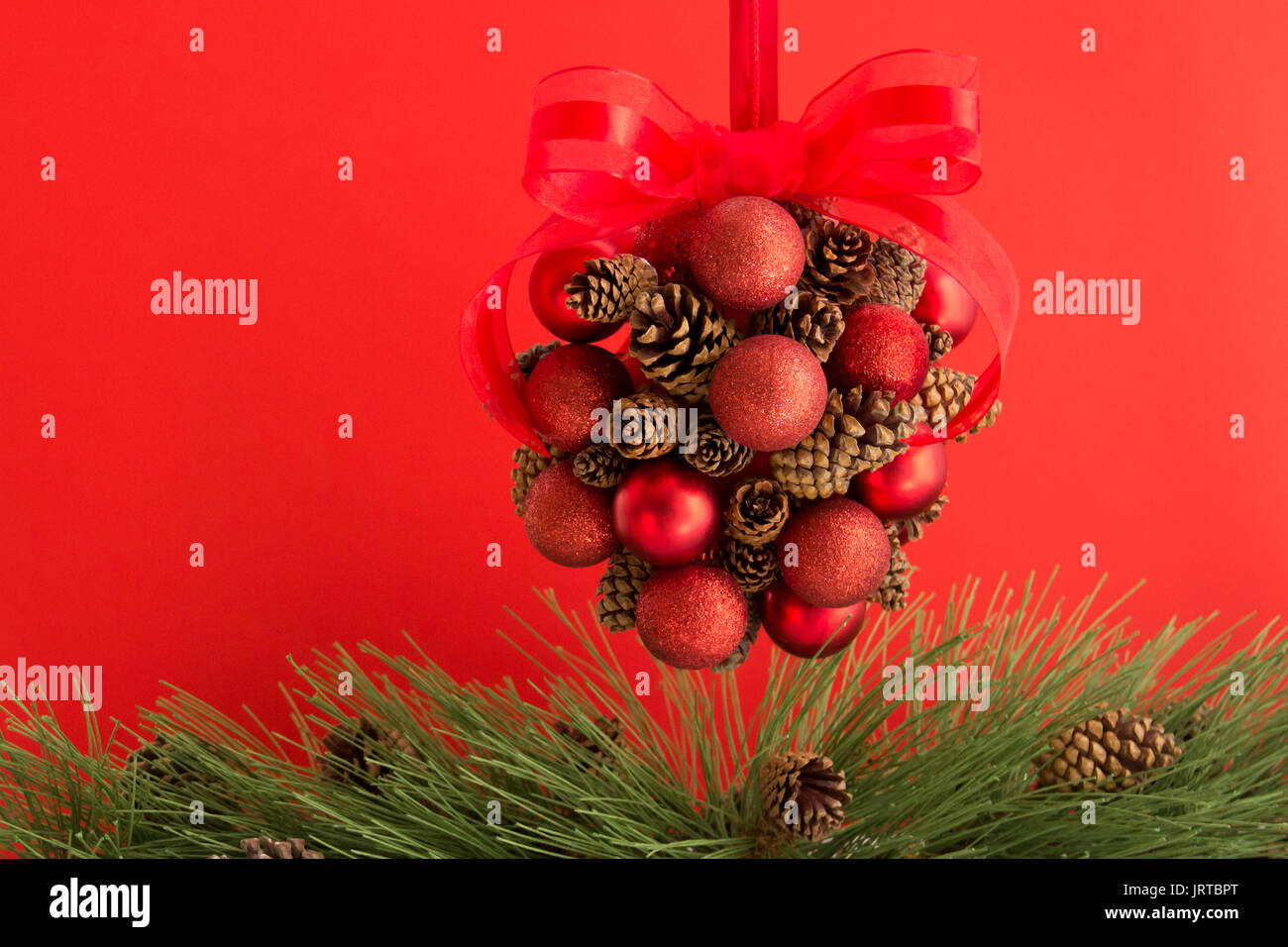 Un cono di pino e sfera rossa appesa decorazione con un rosso organza bow è appeso sopra pino verde con pigne. Foto Stock