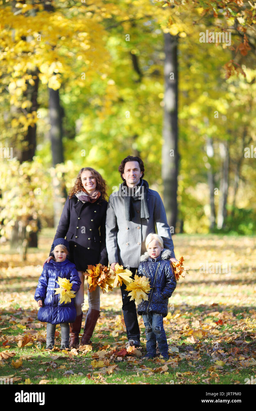 Felice famiglia con due bambini passeggiate nel parco di autunno tenendo le mani Foto Stock