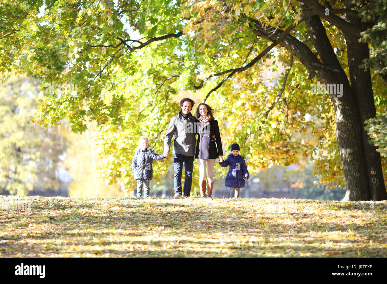 Felice famiglia con due bambini passeggiate nel parco di autunno tenendo le mani Foto Stock