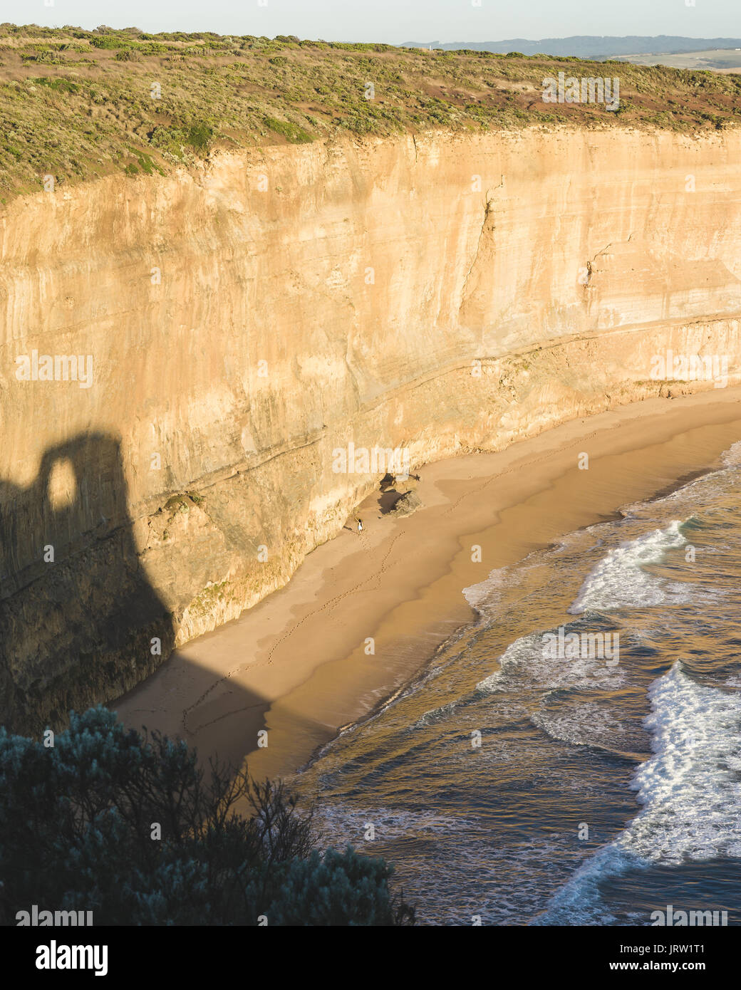 Persona piccola in confronto alle scogliere della Gibson passi della Great Ocean Road nella luce dorata del crepuscolo. Foto Stock