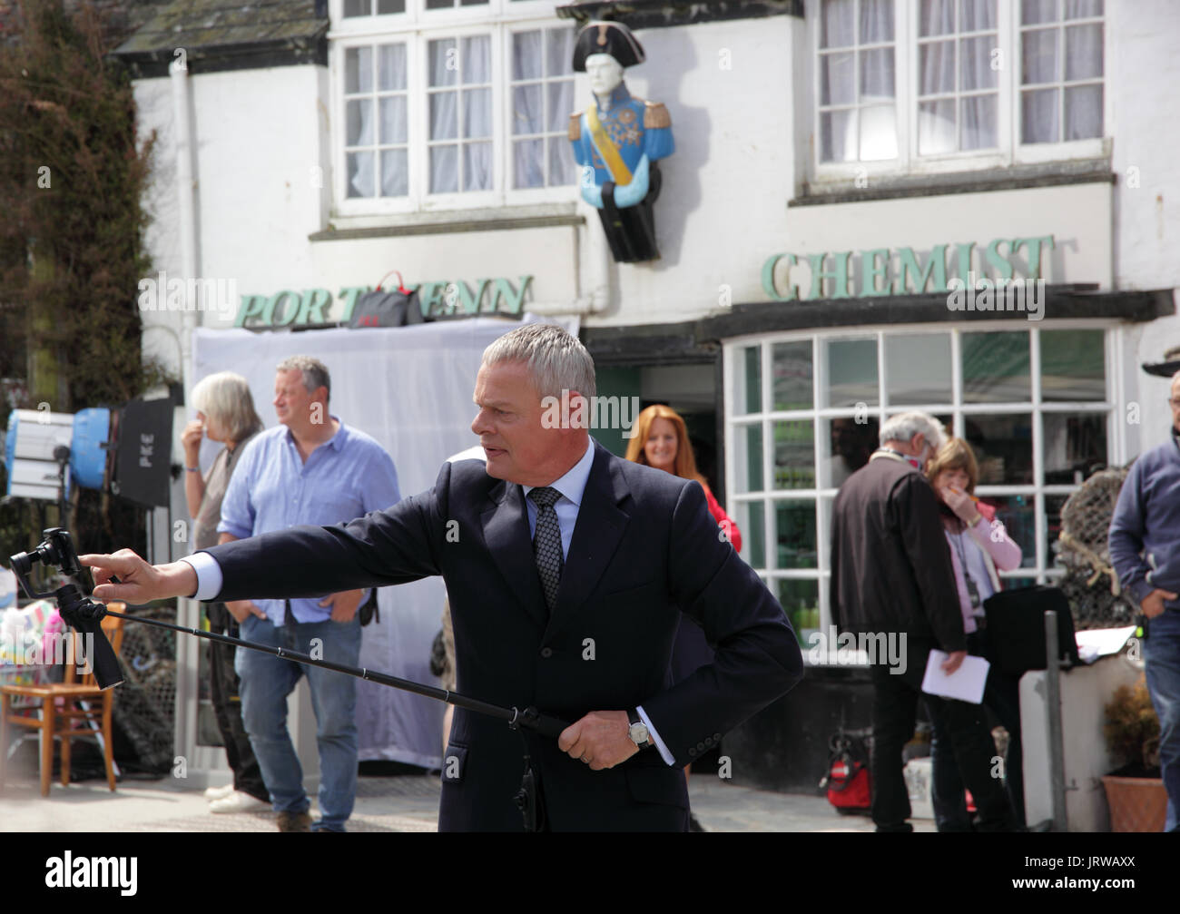 Martin Clunes sulla posizione di ripresa Doc Martin, prendendo il tempo fuori dalle riprese di utilizzare una bacchetta selfie a video la folla Foto Stock