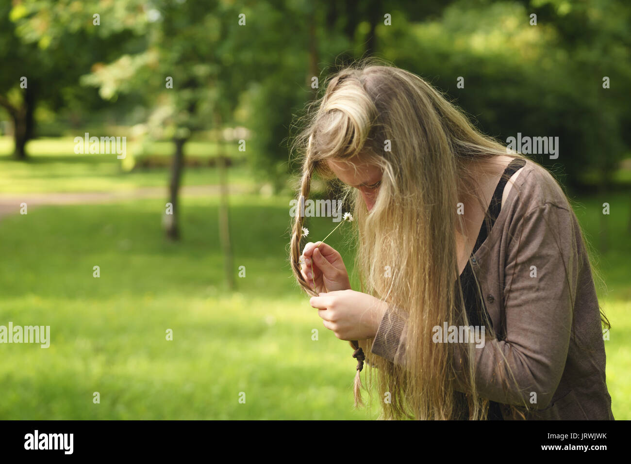 Teen girl allegare daisy fiori nei capelli in parco verde da dietro nel giorno di estate Foto Stock