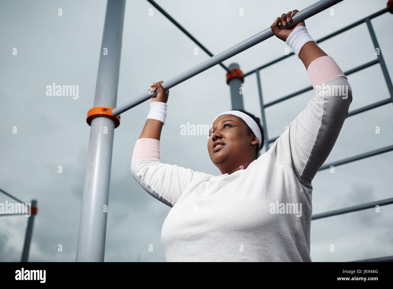 Determinato il sovrappeso donna africana la pratica di pull-up esercizio all'aperto Foto Stock