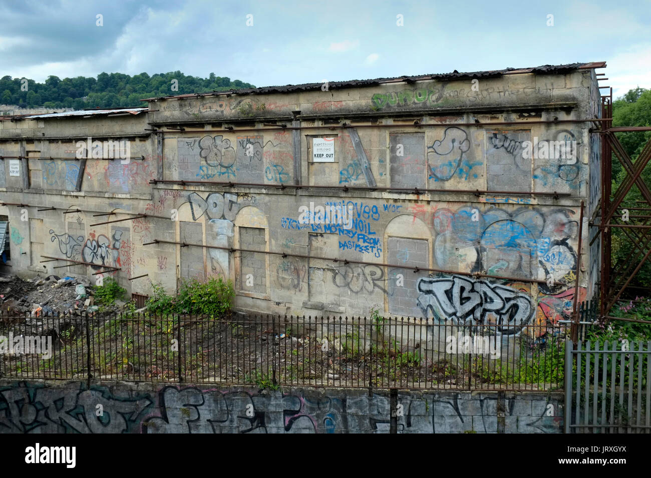 Abbandonata, soggetto ad atti vandalici case con graffiti alla fine della fila di Hampton nel centro della città di Bath, Regno Unito, con un ponte pedonale che attraversa il principale di Londra Foto Stock