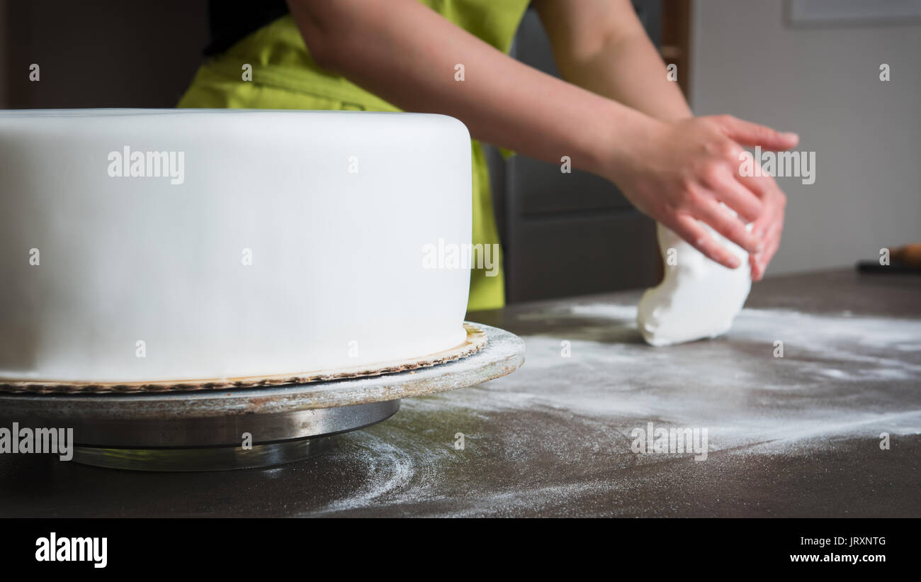 Irriconoscibile donna preparazione fondente bianco per la decorazione delle torte, mani dettaglio, concentrarsi sulla torta Foto Stock