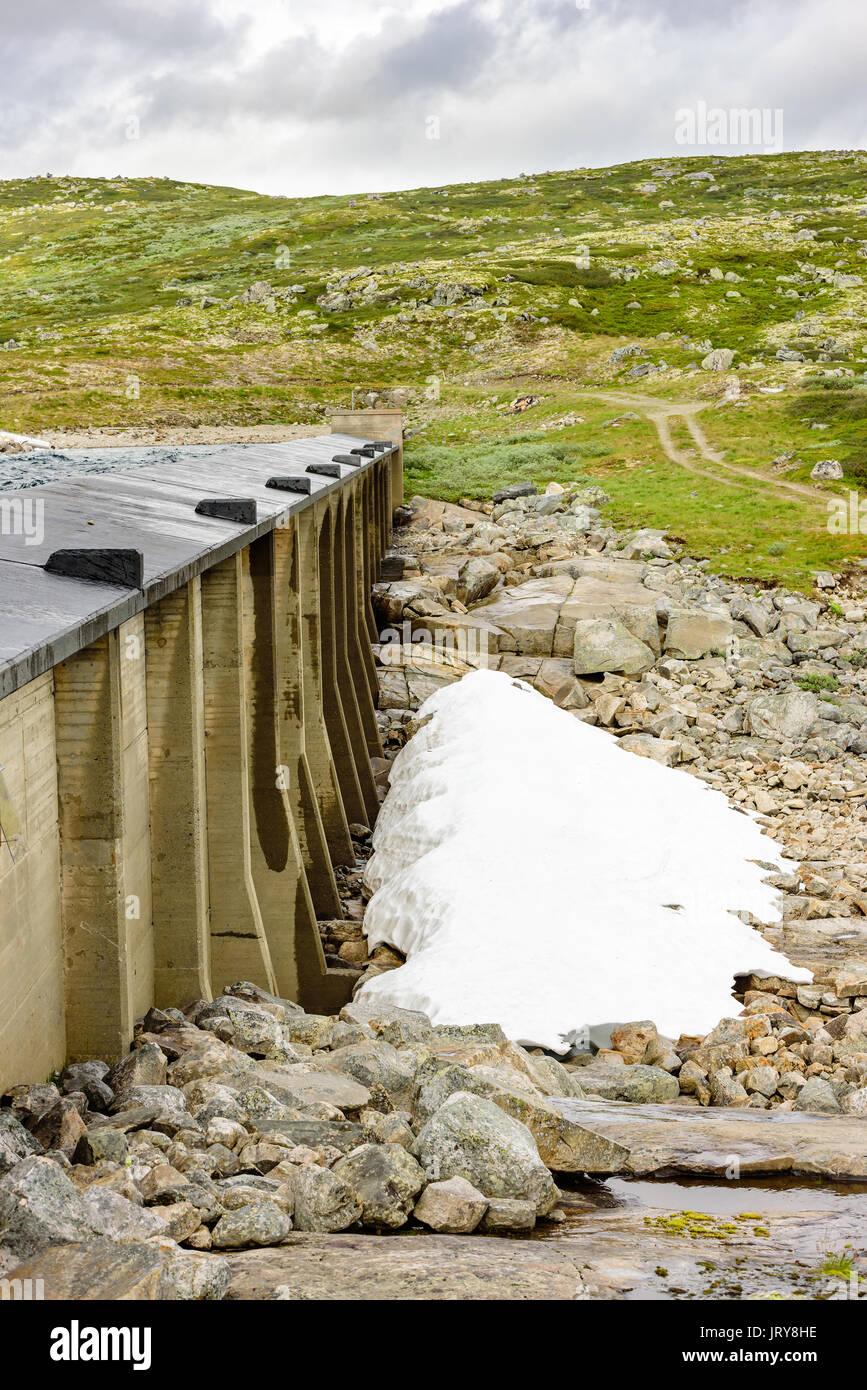 Piccolo mucchio di neve sotto la parete in calcestruzzo della diga o al serbatoio di acqua nel paesaggio delle highland. Foto Stock