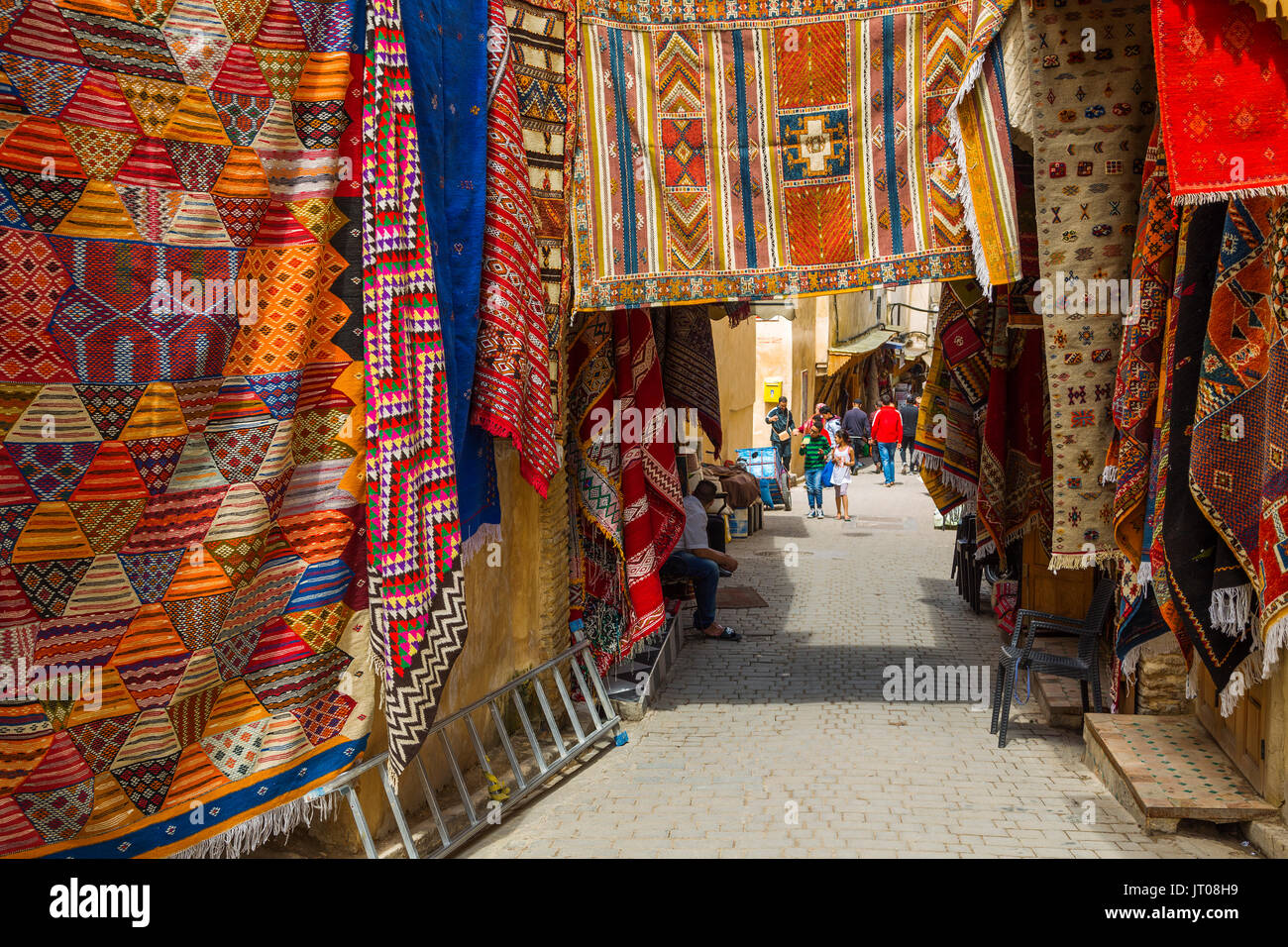 La vita di strada scena. Tappeti con motivi tradizionali per la vendita in un mercato di souq, bazaar. Souk Medina di Fez, Fes el Bali. Il Marocco, Maghreb Nord Africa Foto Stock