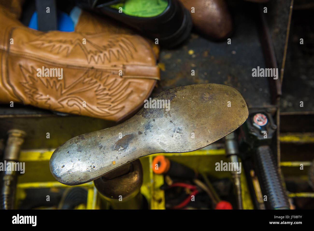 Foto ravvicinate degli attrezzi per la riparazione delle scarpe e delle calzature in un'officina tradizionale di ciabattine, mettendo in evidenza le suole, le attrezzature per la riparazione e il processo di risolina Foto Stock