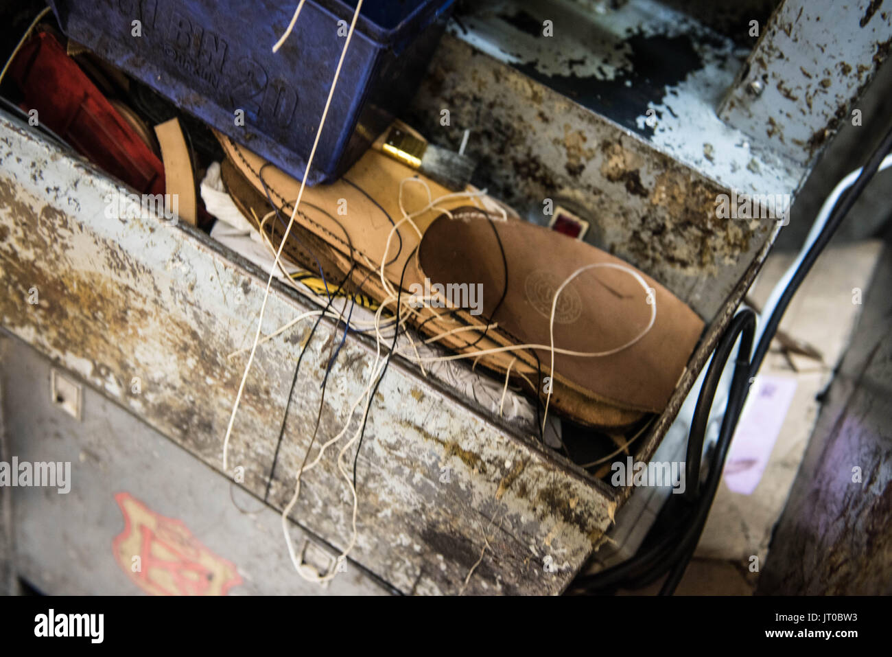 Foto ravvicinate degli attrezzi per la riparazione delle scarpe e delle calzature in un'officina tradizionale di ciabattine, mettendo in evidenza le suole, le attrezzature per la riparazione e il processo di risolina Foto Stock