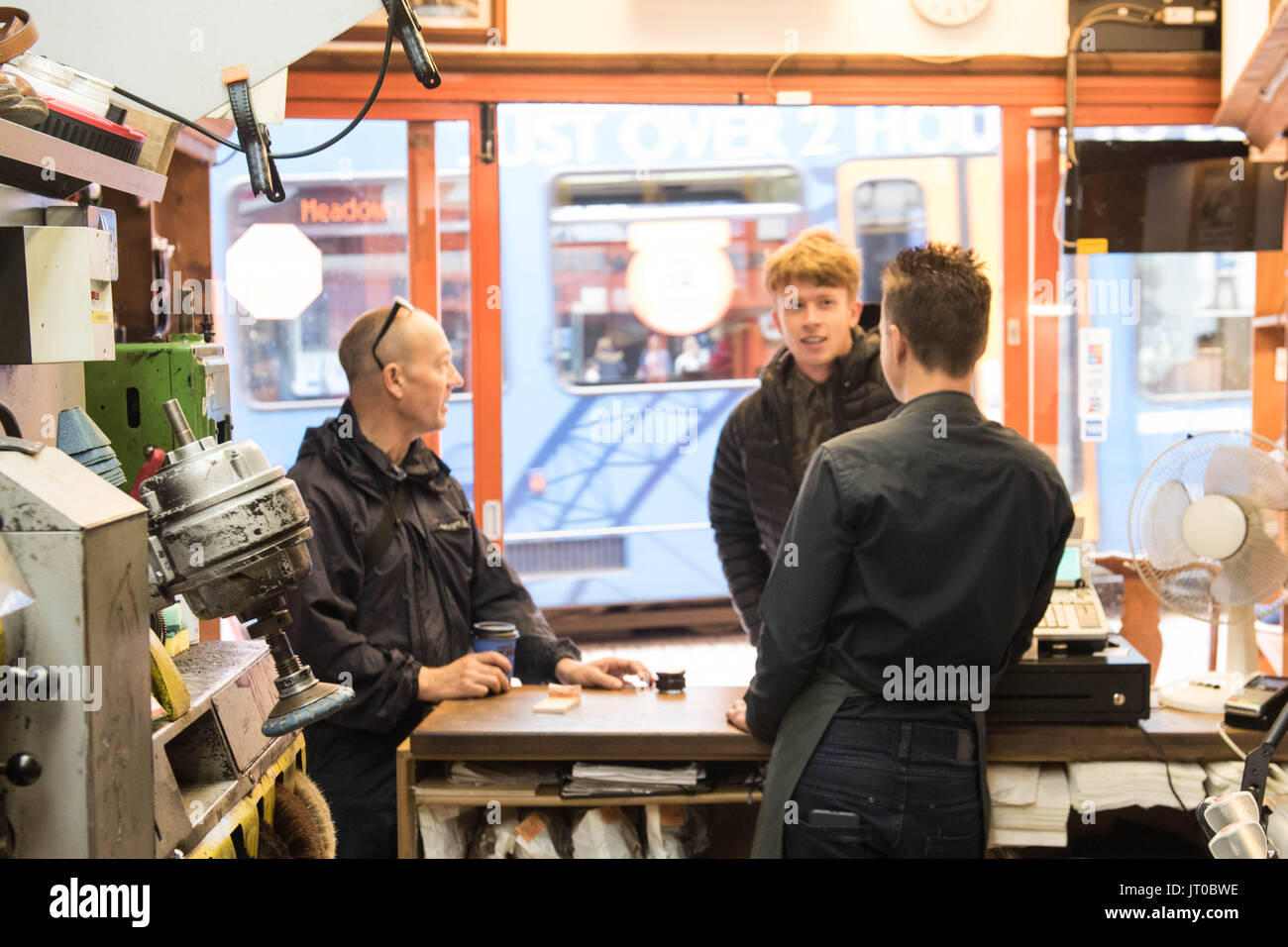 Cobbler che ripara scarpe in pelle all'interno di un'officina tradizionale. Sulla parete sono visibili utensili, attrezzature di taglio chiave e suole di ricambio Foto Stock
