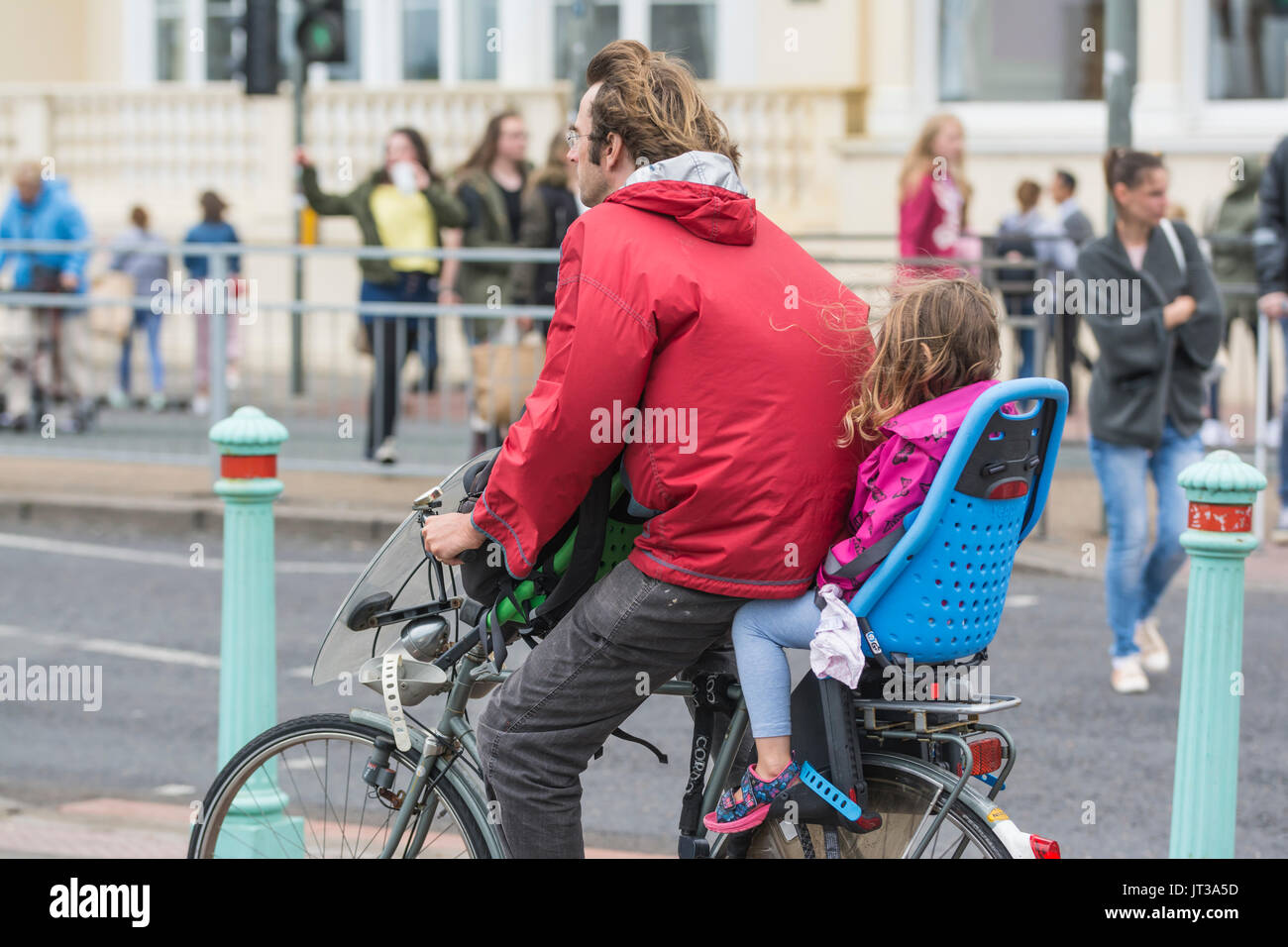 Uomo in bicicletta con un bambino in un sedile per bambini, entrambi non indossa un casco. Ciclista irresponsabile. Foto Stock
