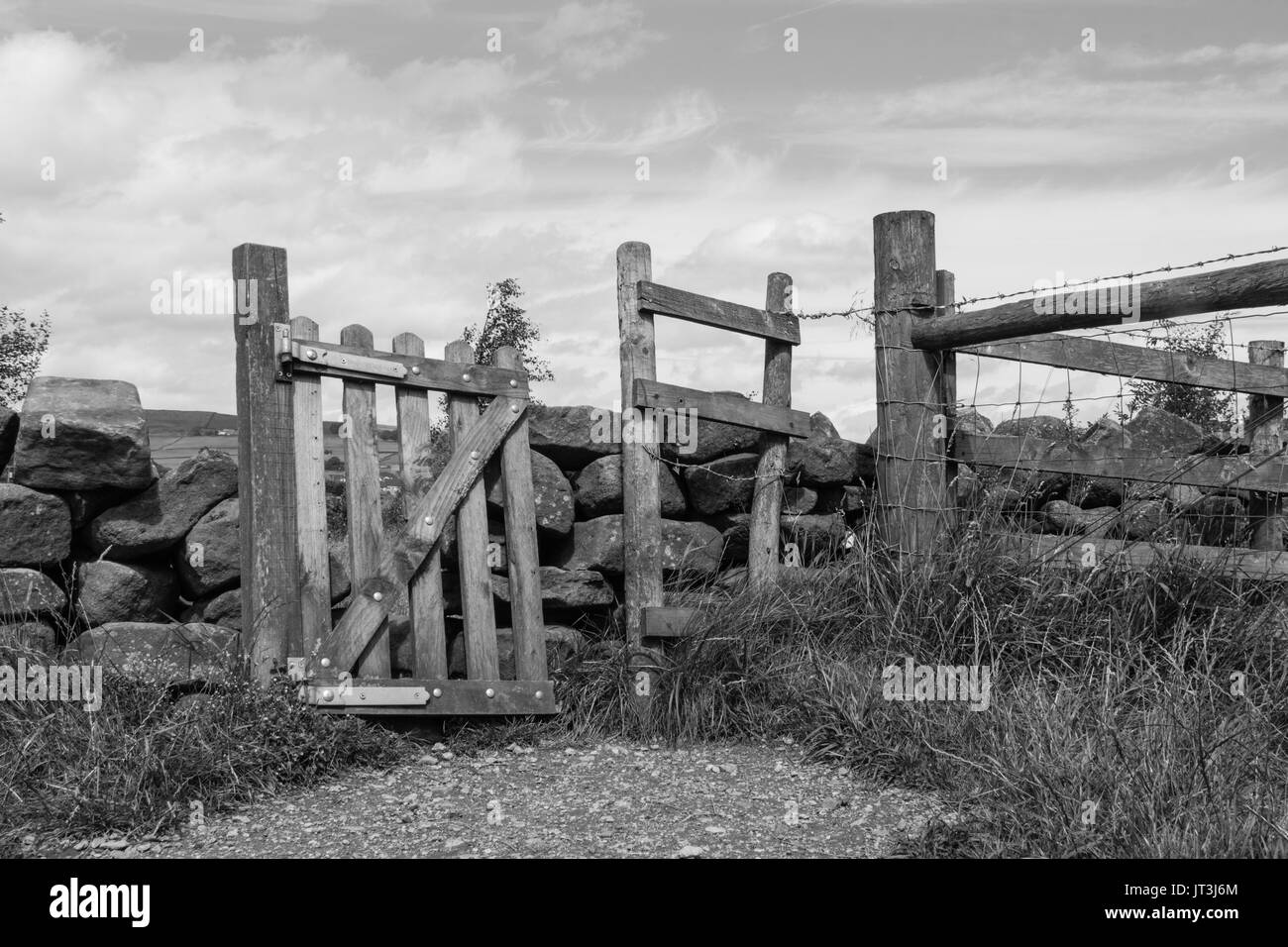 Un rustico, obliquo cancello di legno in un tradizionale muro di pietra che separa i campi in zone rurali lancashire campagna. in bianco e nero Foto Stock