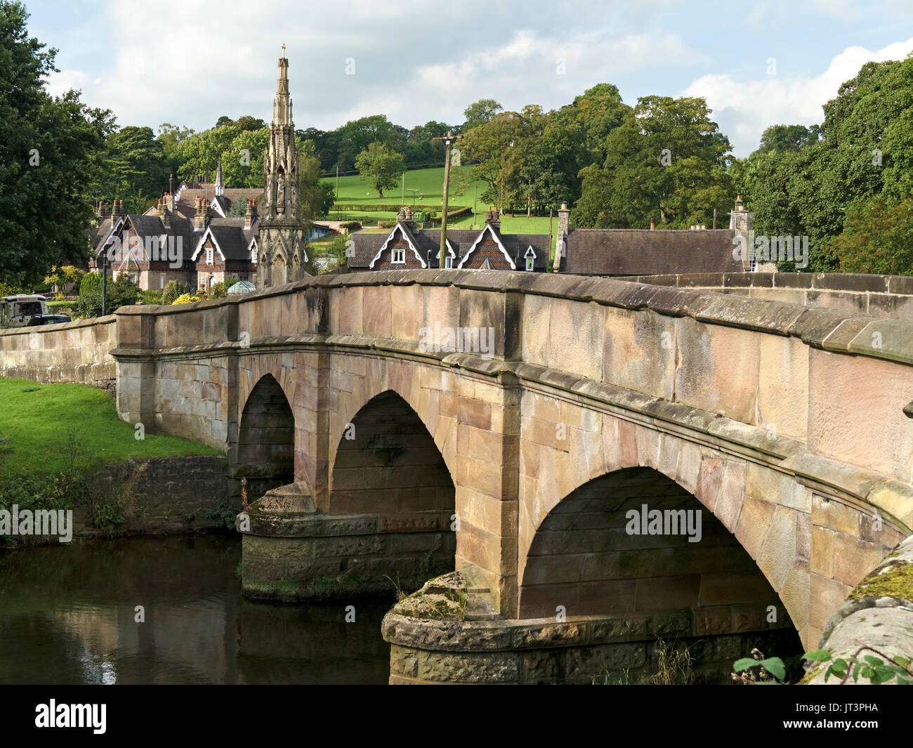 Arco in pietra ponte sul fiume il collettore con il villaggio di Ilam oltre, Derbyshire, England, Regno Unito Foto Stock