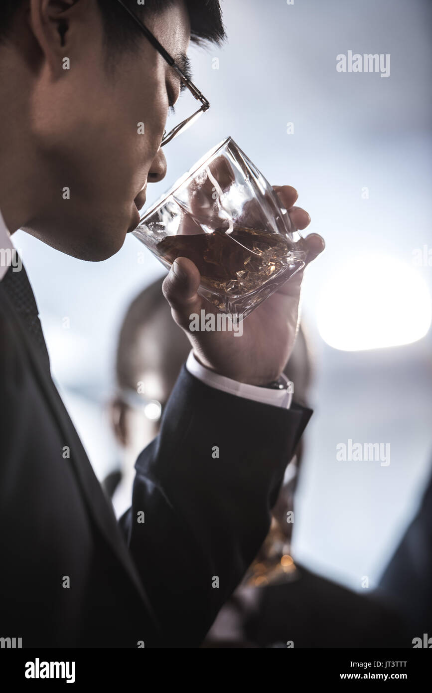 Vista ravvicinata di imprenditore asiatici in occhiali di bere whisky dal vetro Foto Stock