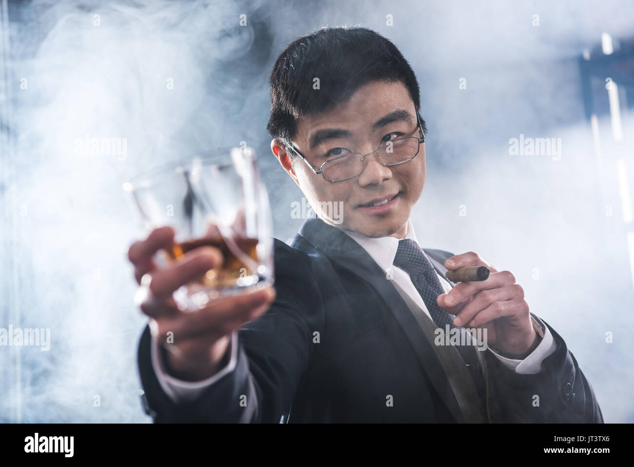 Vista ravvicinata di fiducioso imprenditore asiatico di bere whisky e fumare il sigaro Foto Stock