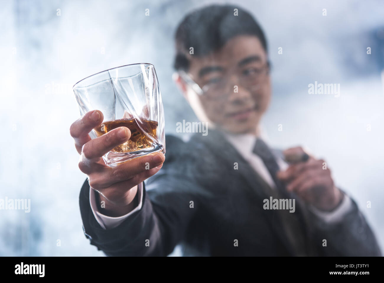 Vista ravvicinata di fiducioso imprenditore asiatico di bere whisky e fumare il sigaro Foto Stock