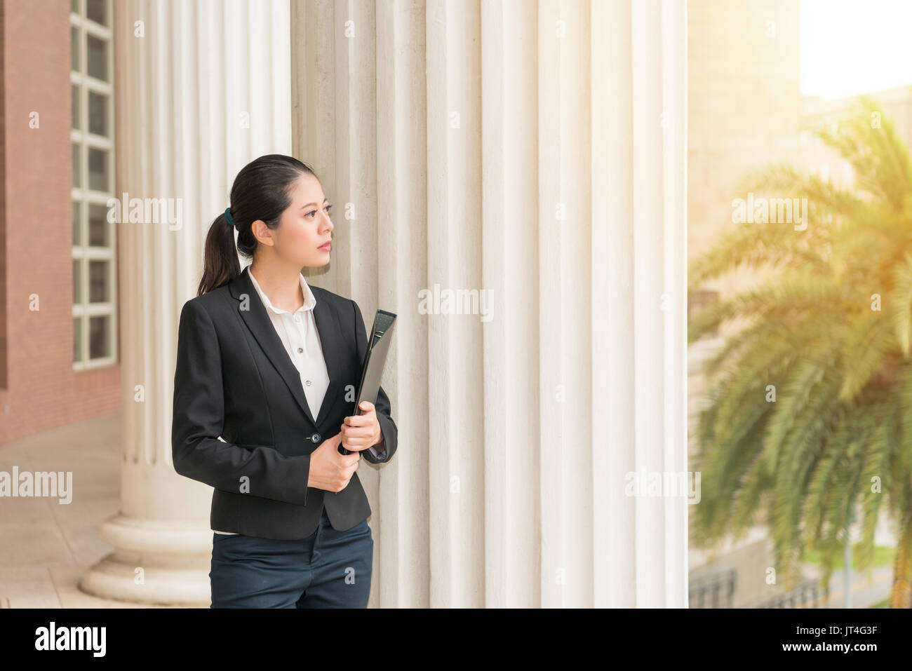 Professional femmina giovane avvocato in piedi accanto alla classica corte palazzo colonna fascio pensando di azione legale casi risolvere il problema per aiutare customer Foto Stock