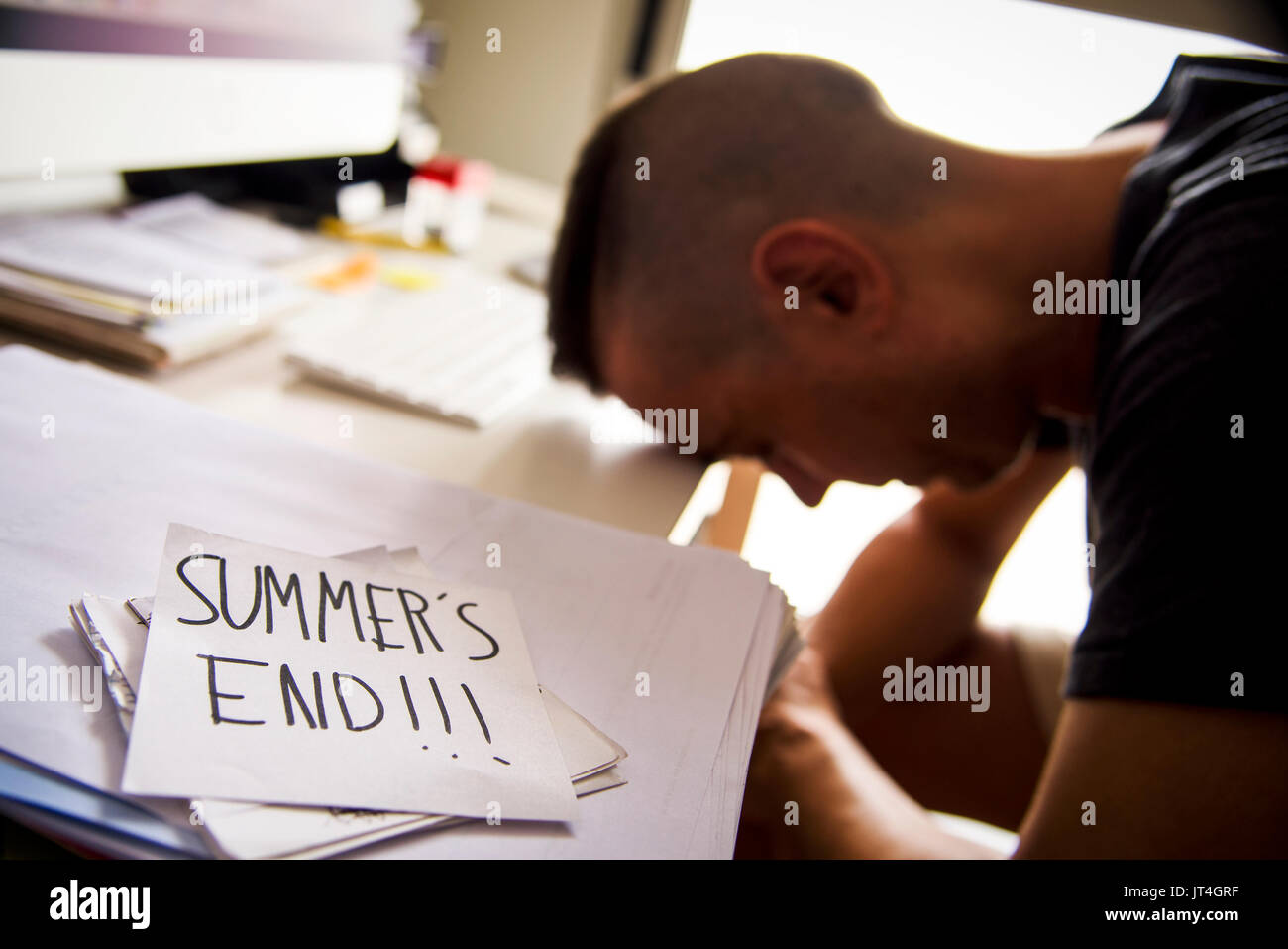 Primo piano di un interessato l'uomo seduto alla sua scrivania in ufficio e una nota in primo piano con il testo estati manoscritte di estremità in esso Foto Stock