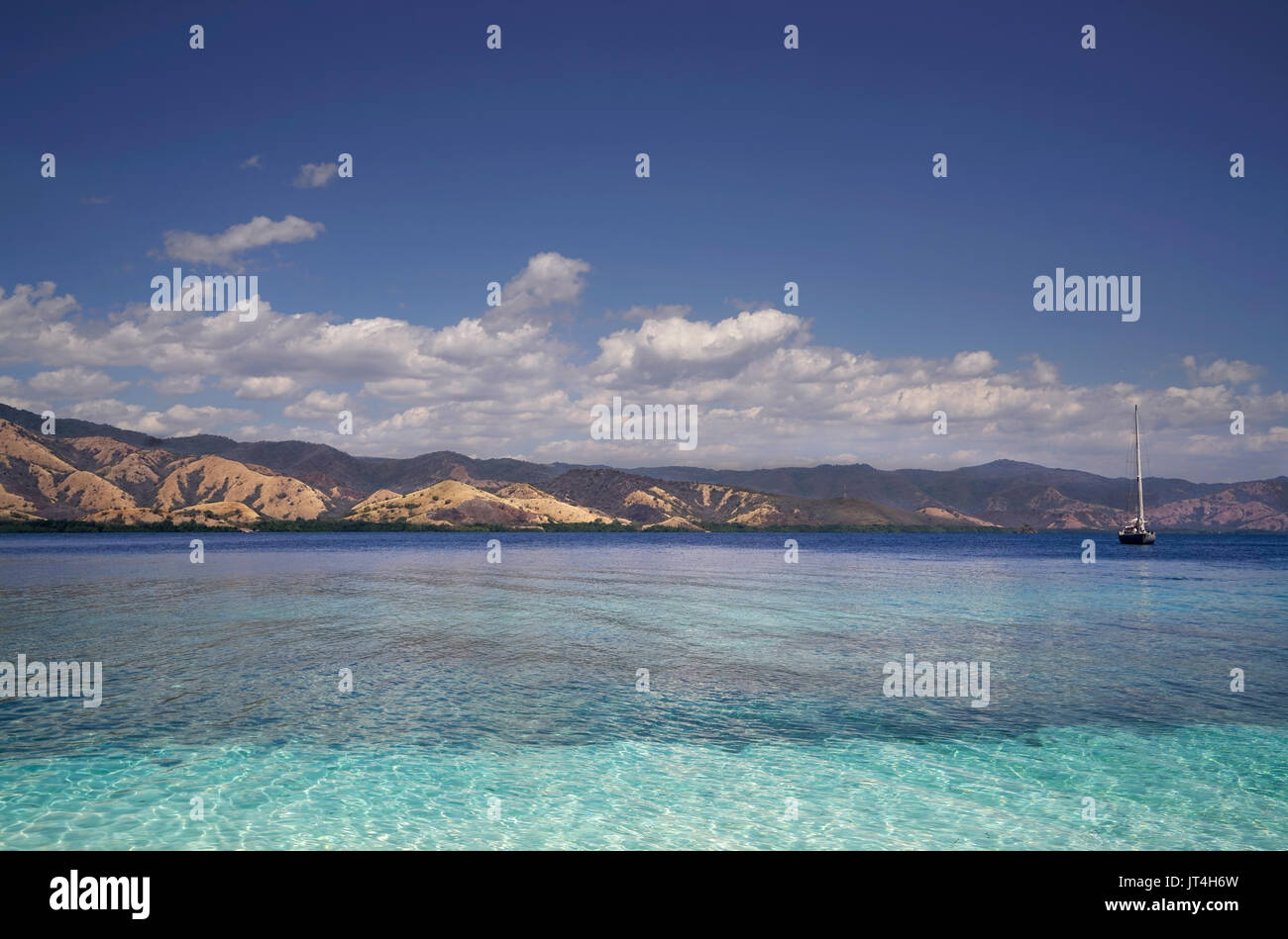In barca a vela su trasparente blu oceano tropicale di acqua durante la giornata con ampia isola verde dietro, Flores Indonesia. Foto Stock